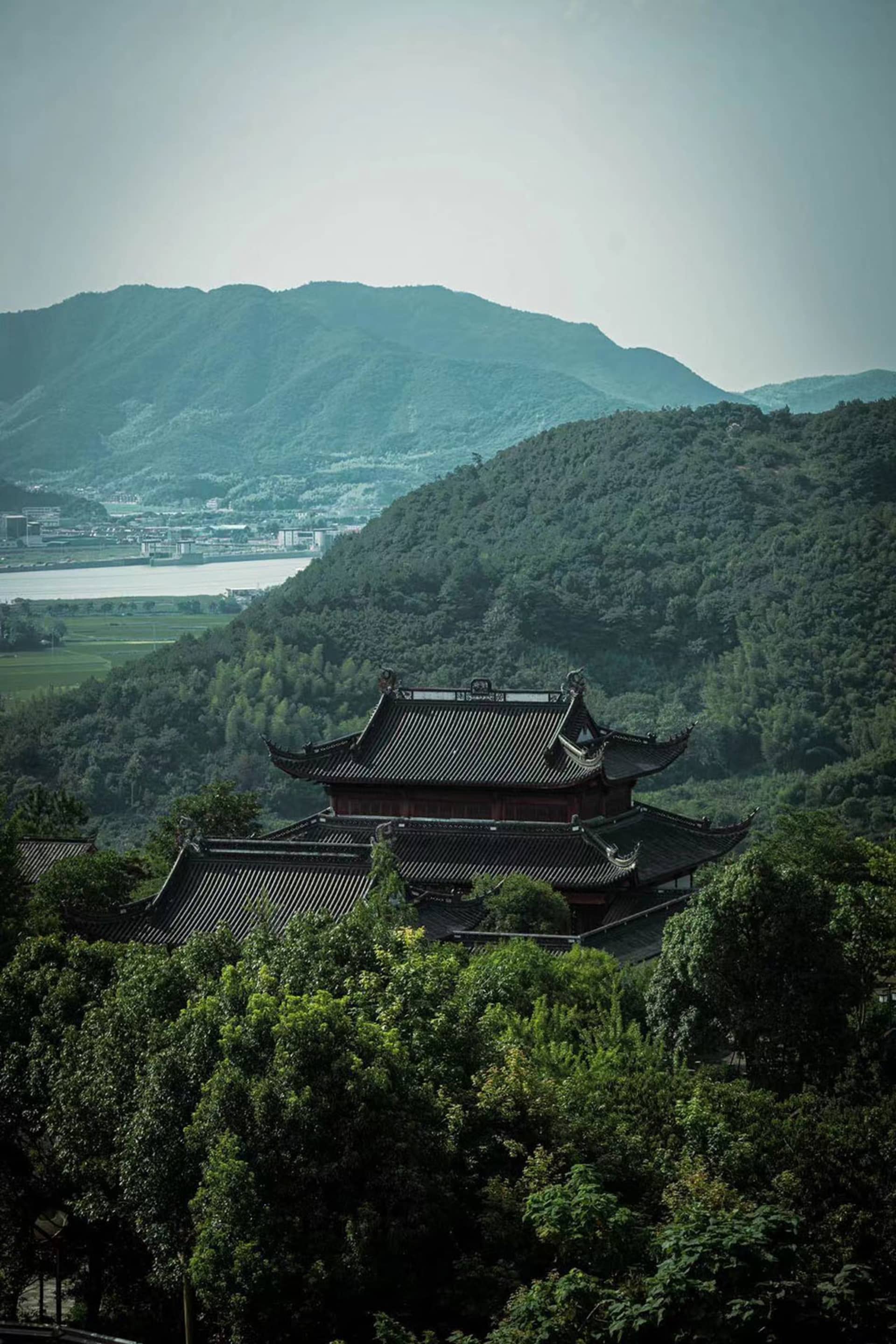 A traditional architectural structure situated amidst lush green hills and mountains, surrounded by trees.