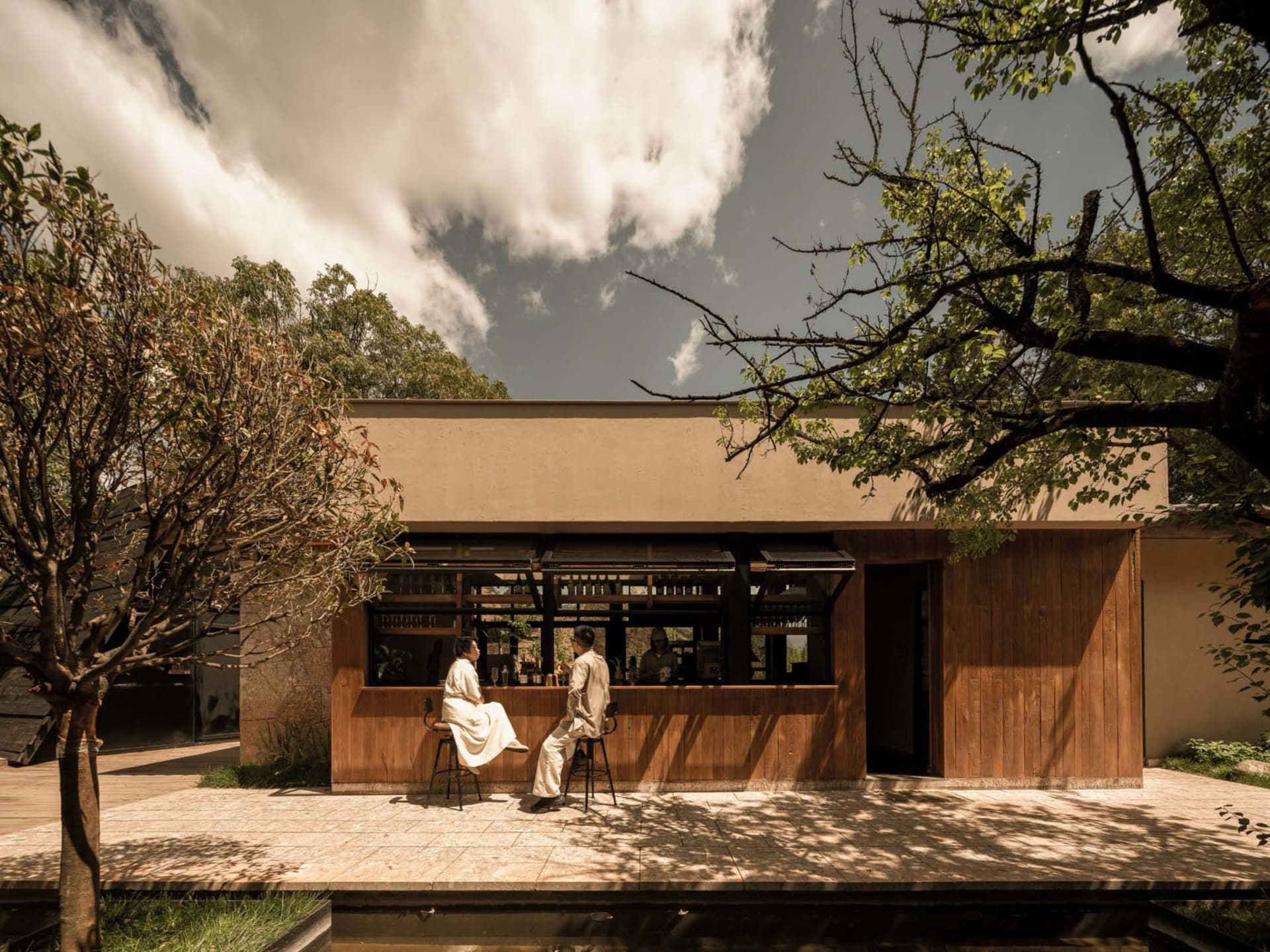 People enjoying drinks at a minimalist cafe with wooden features and outdoor seating.