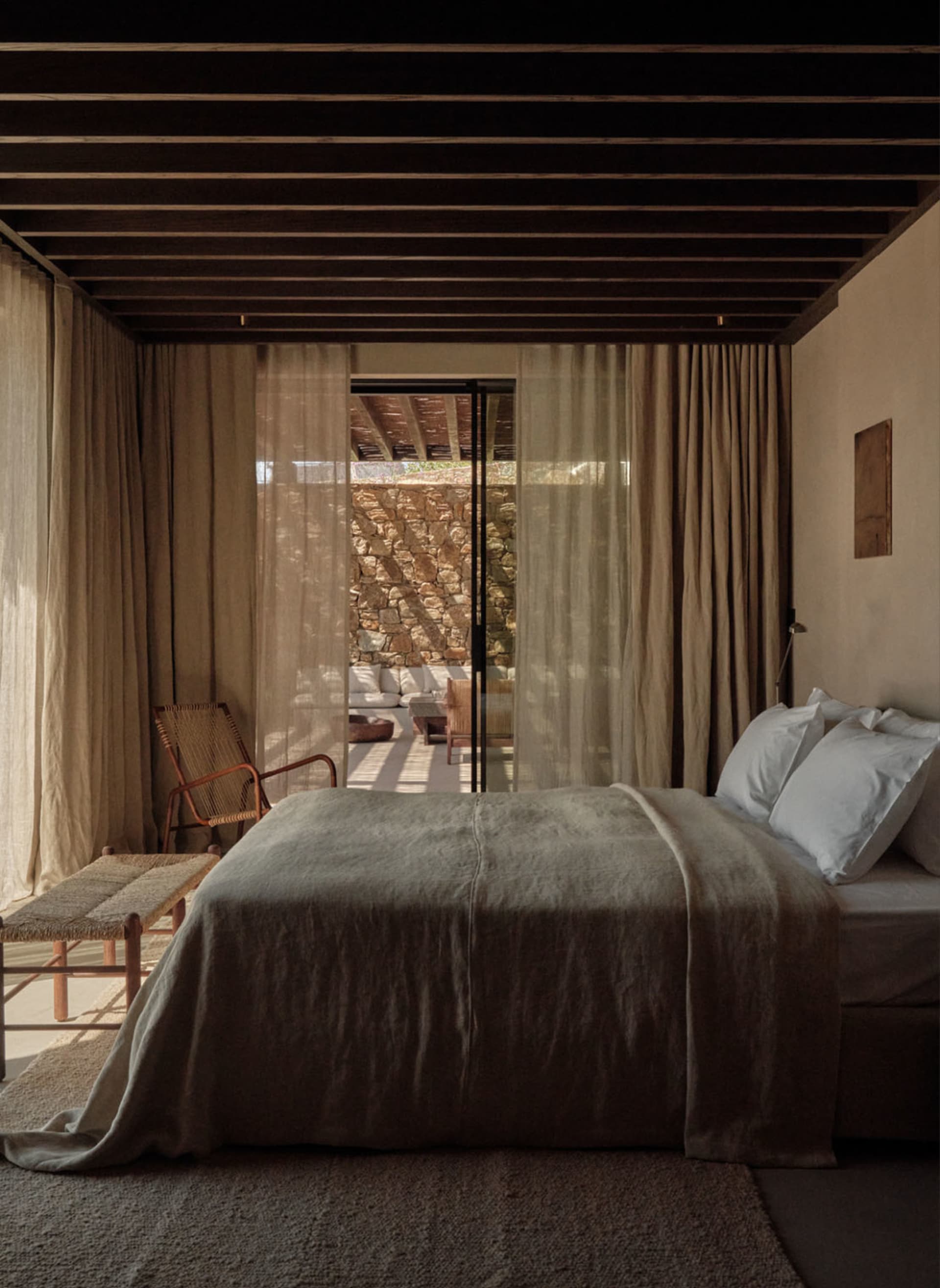 A bedroom with a simple, modern design featuring organic wooden furniture and light fabric textiles.
