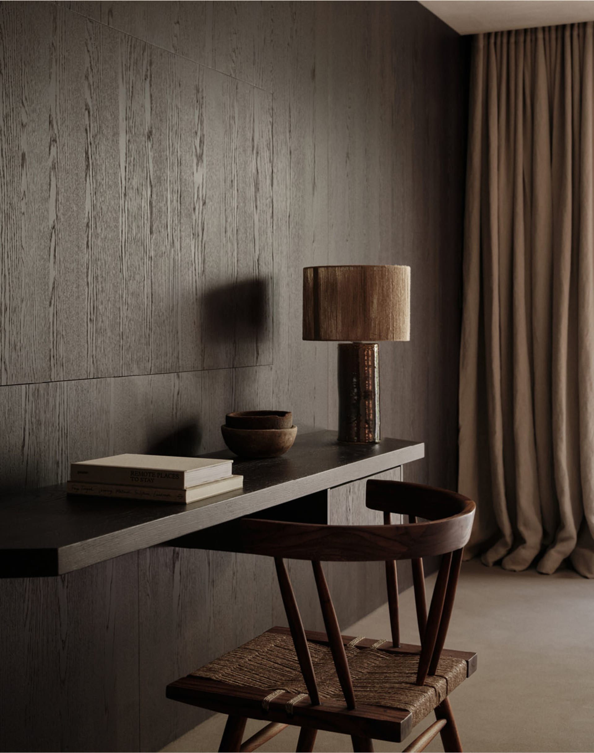A modern home office desk with a wooden chair, lamp, and a few books.