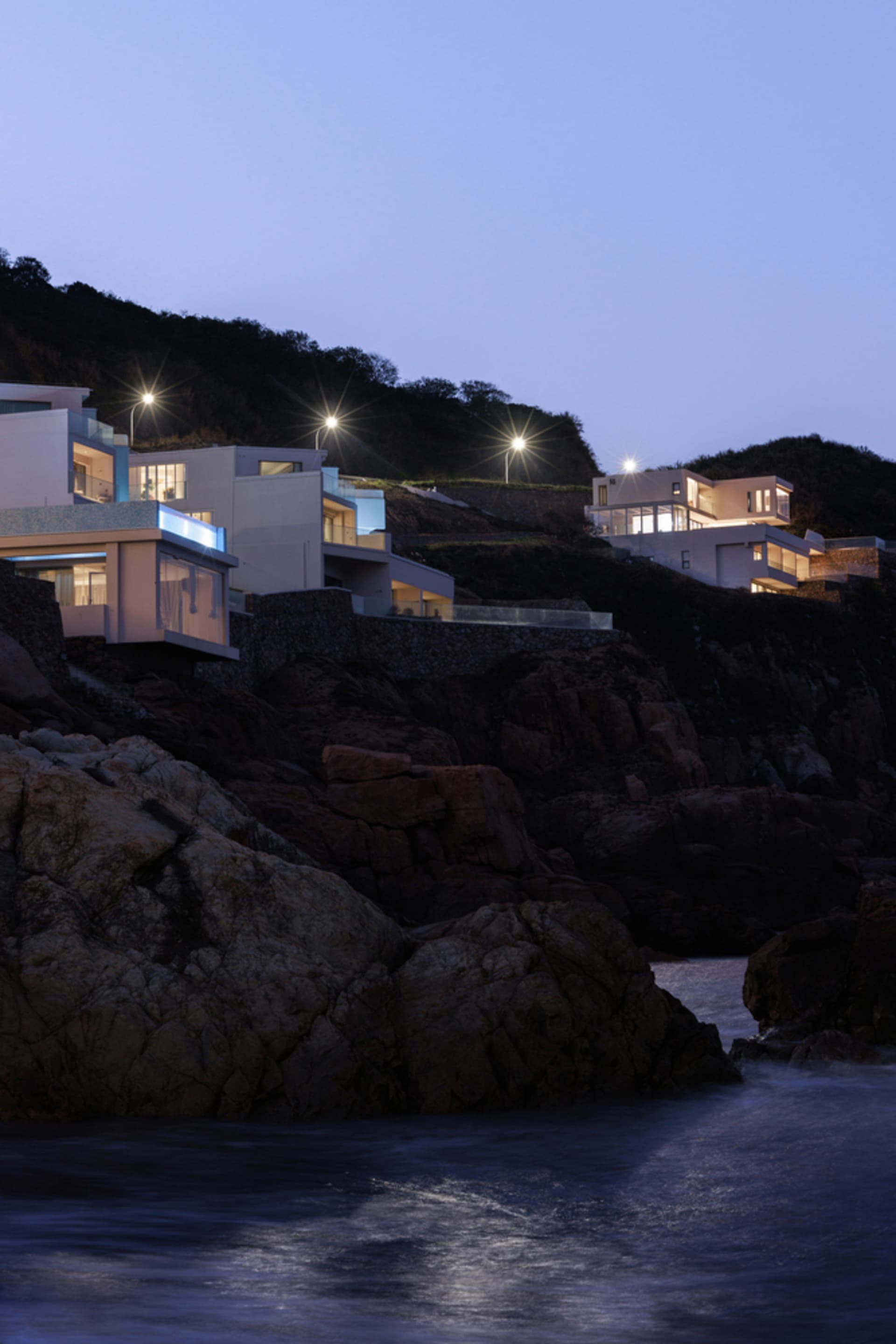 Modern residential houses constructed of concrete, illuminated at dusk with lights on.