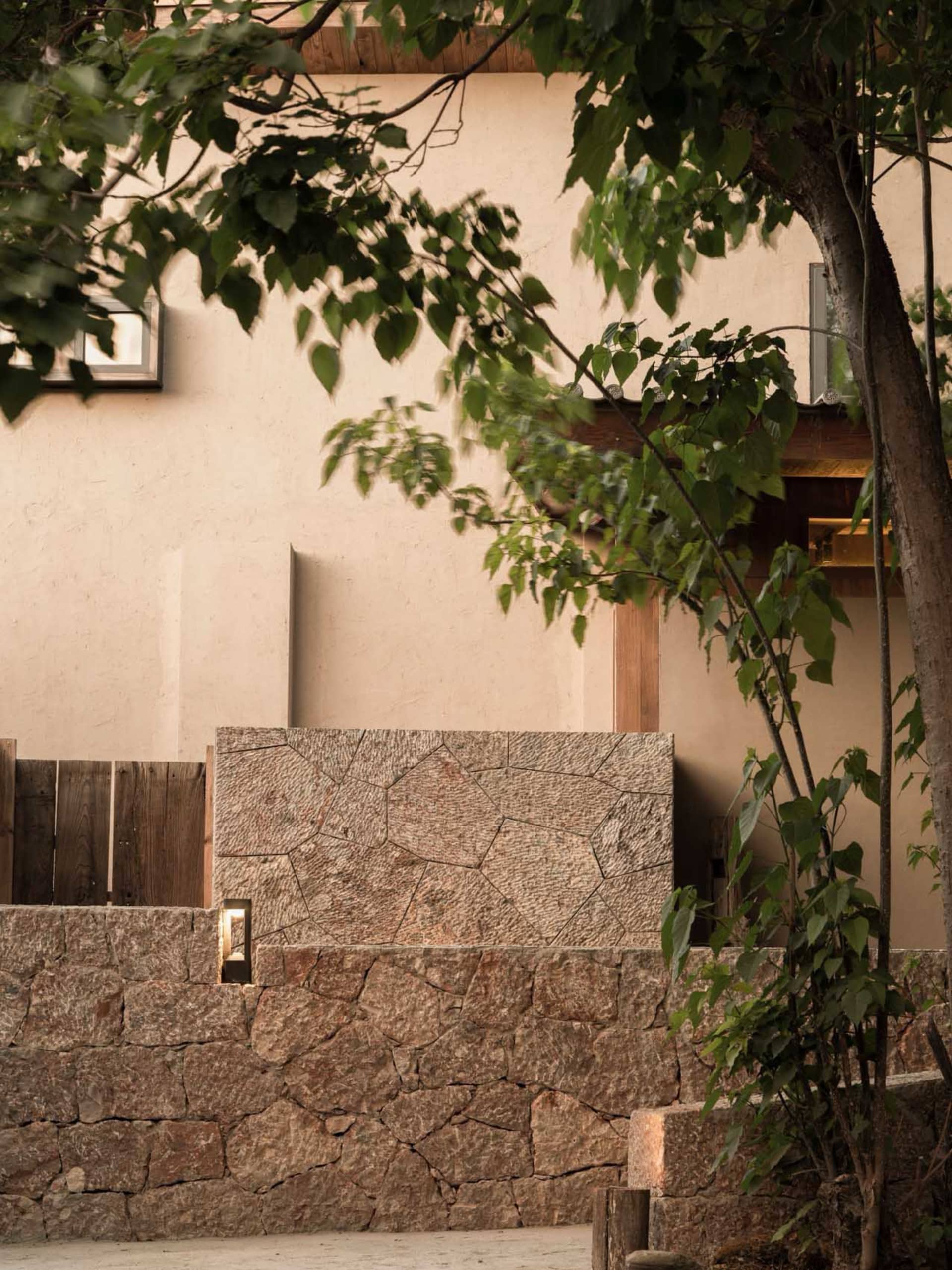 Modern residential exterior featuring a stone-clad wall and surrounding greenery.