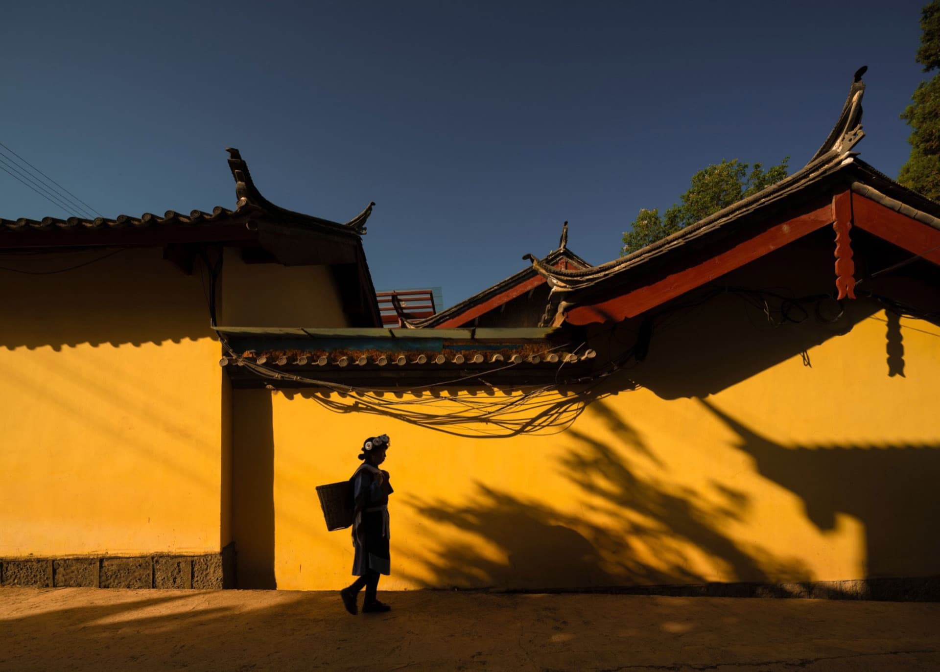 A person walking past a traditional Chinese building with a yellow wall and clay tiles.