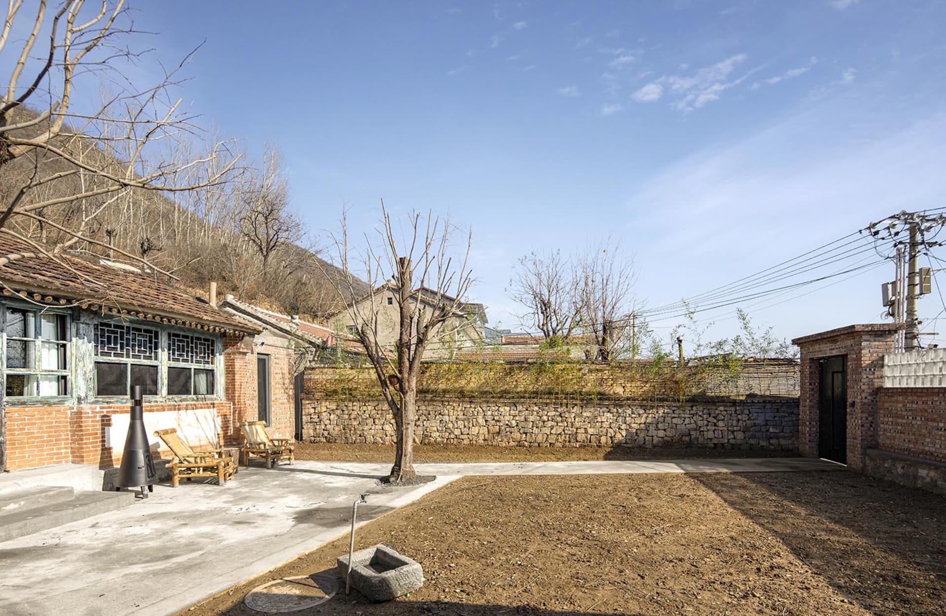 A traditional brick residential home with a stone wall and dry grass field.