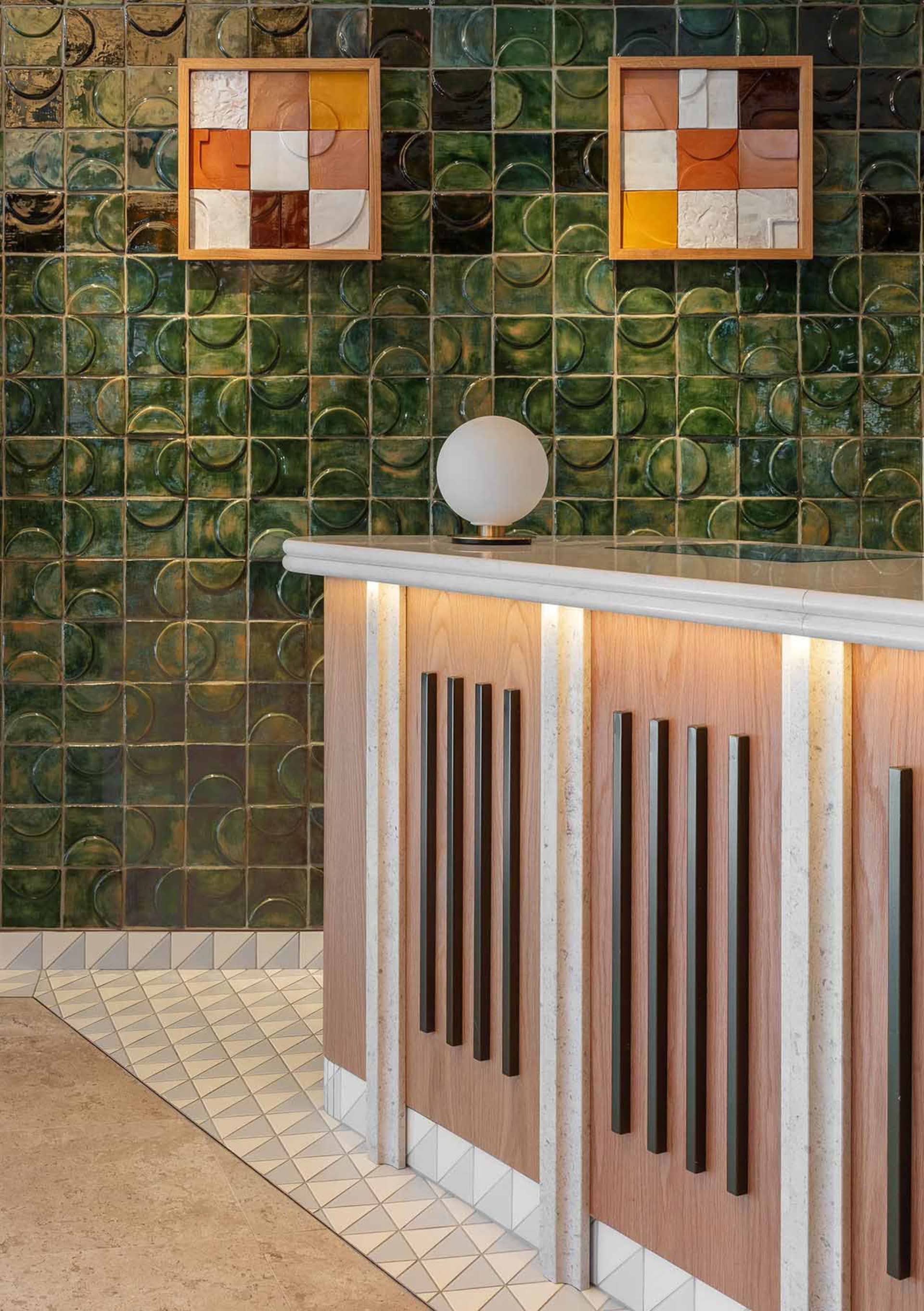 A modern commercial reception area featuring sleek wooden cabinets with black handles, a white countertop, and green ceramic