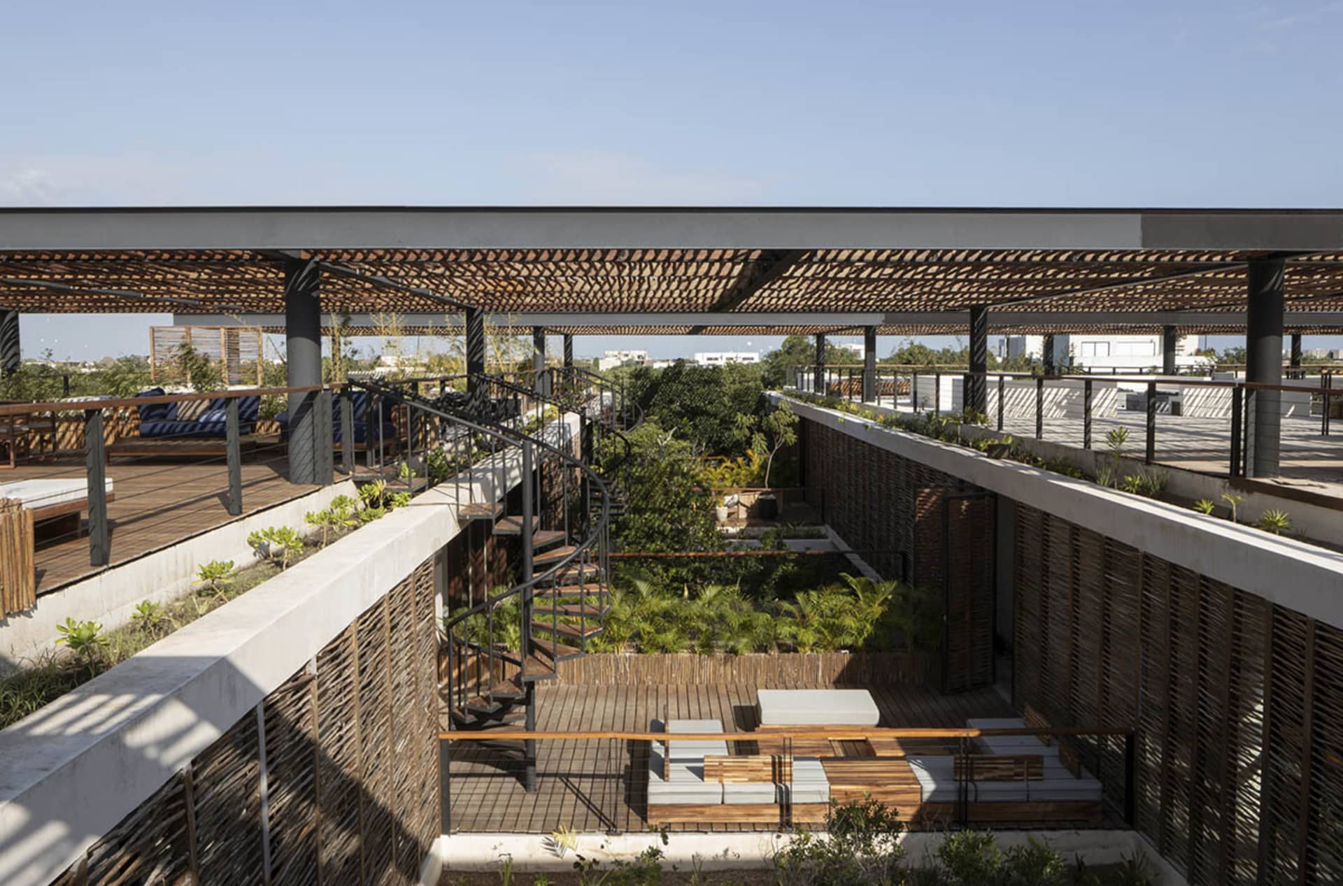 A modern indoor garden featuring wooden railings, concrete flooring, and metal stairs with greenery surrounding the area.