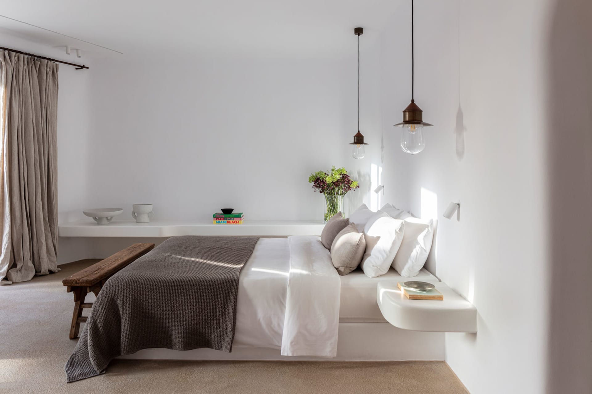 Modern minimalist bedroom featuring a concrete floating bed, white bedding, and minimalist decor.