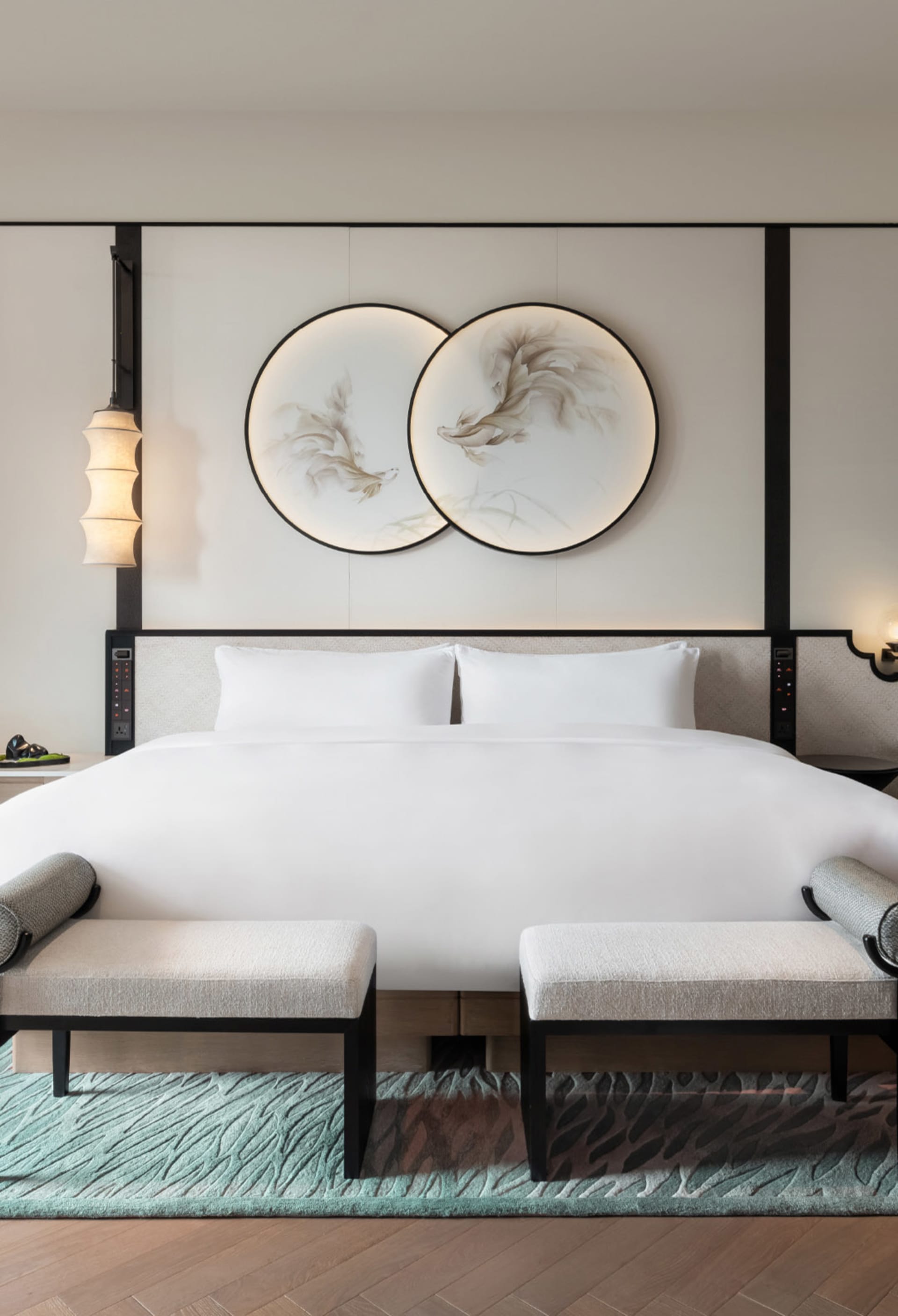 A minimalist bedroom featuring a bed with white textiles, mounted artworks on the wall, and a wooden floor with metal accents