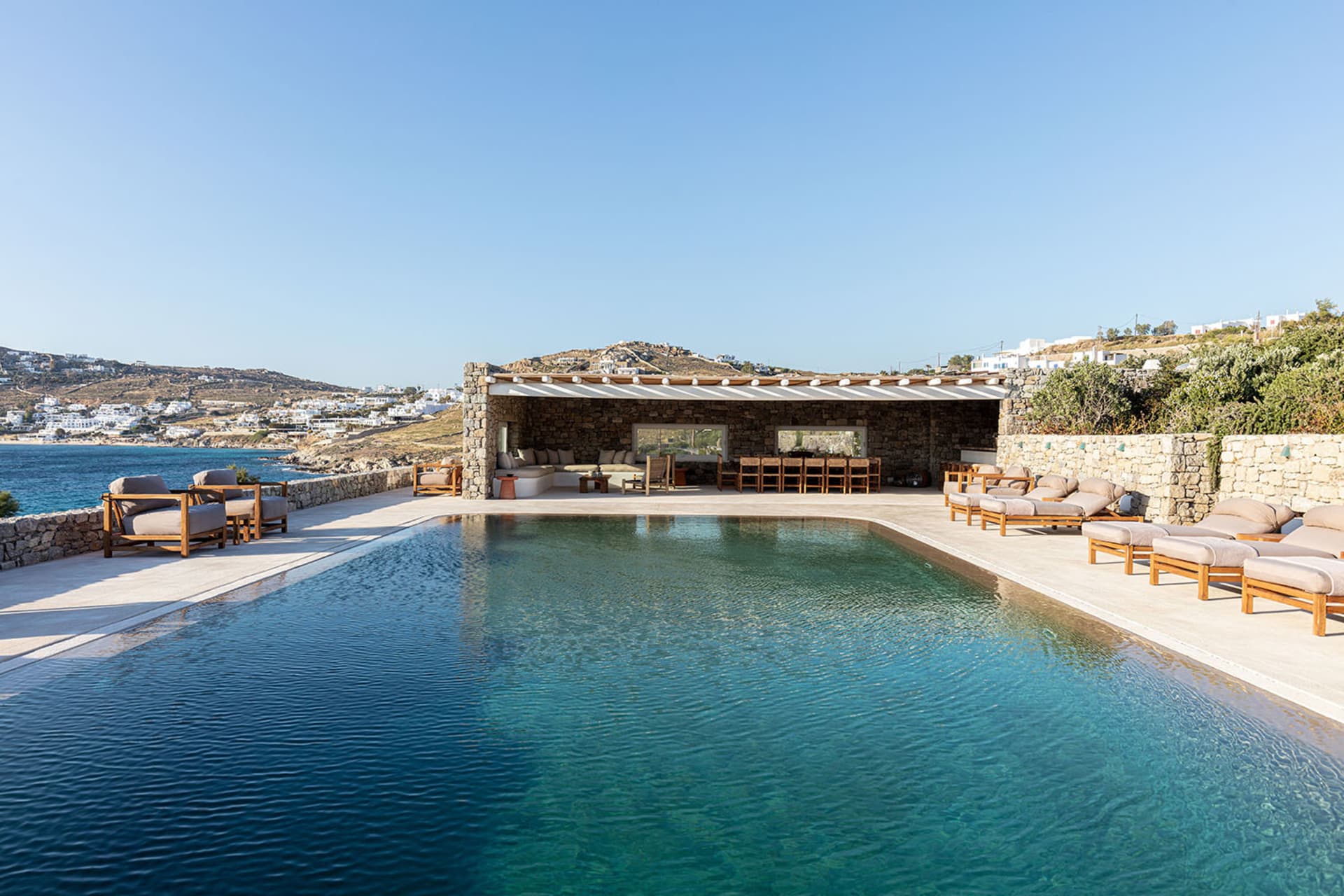 A modern, minimalist residential space featuring a concrete pool and outdoor seating area with a view of the sea.