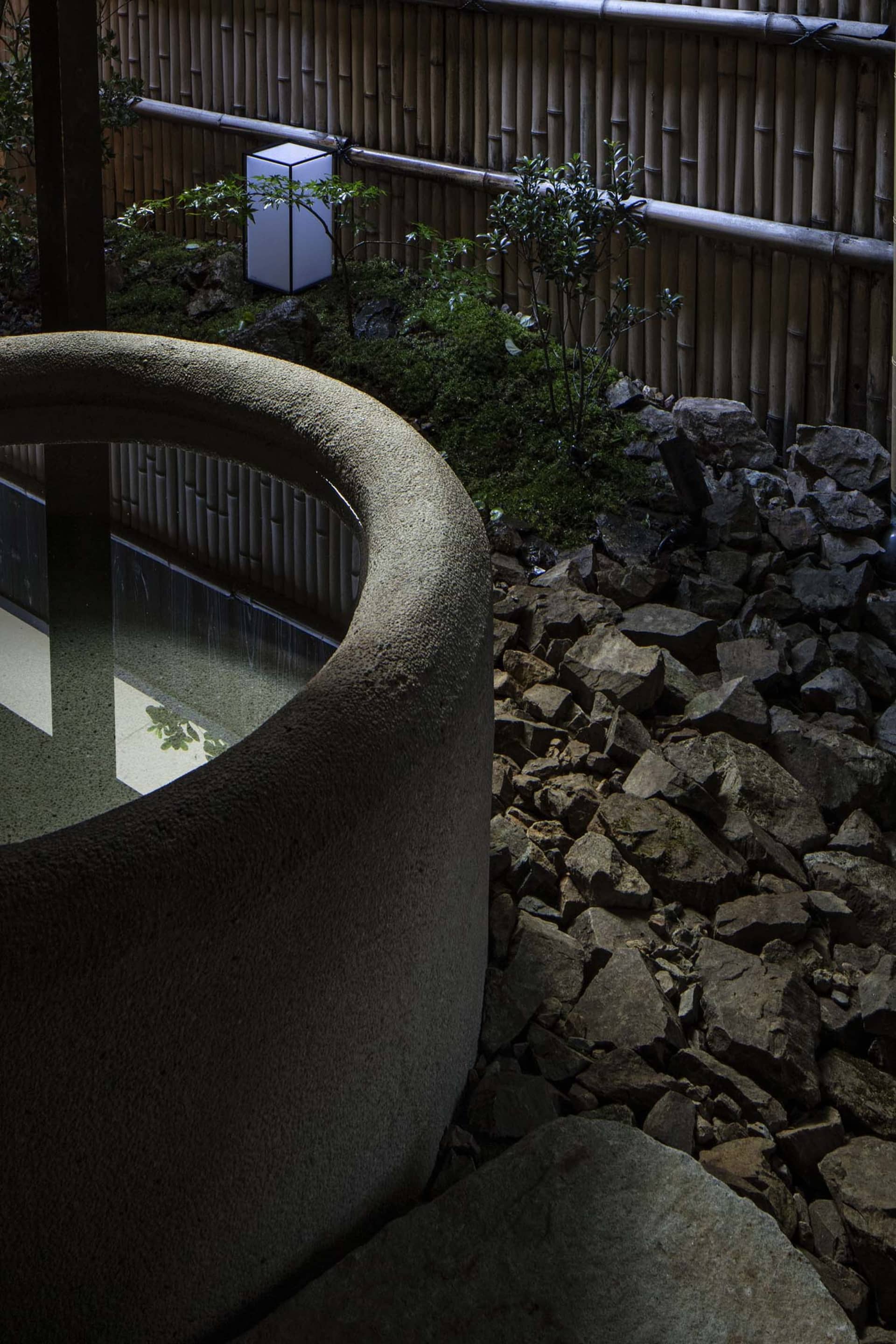 Photograph of a stone garden with bamboo and rock formations, featuring a lantern and water feature.