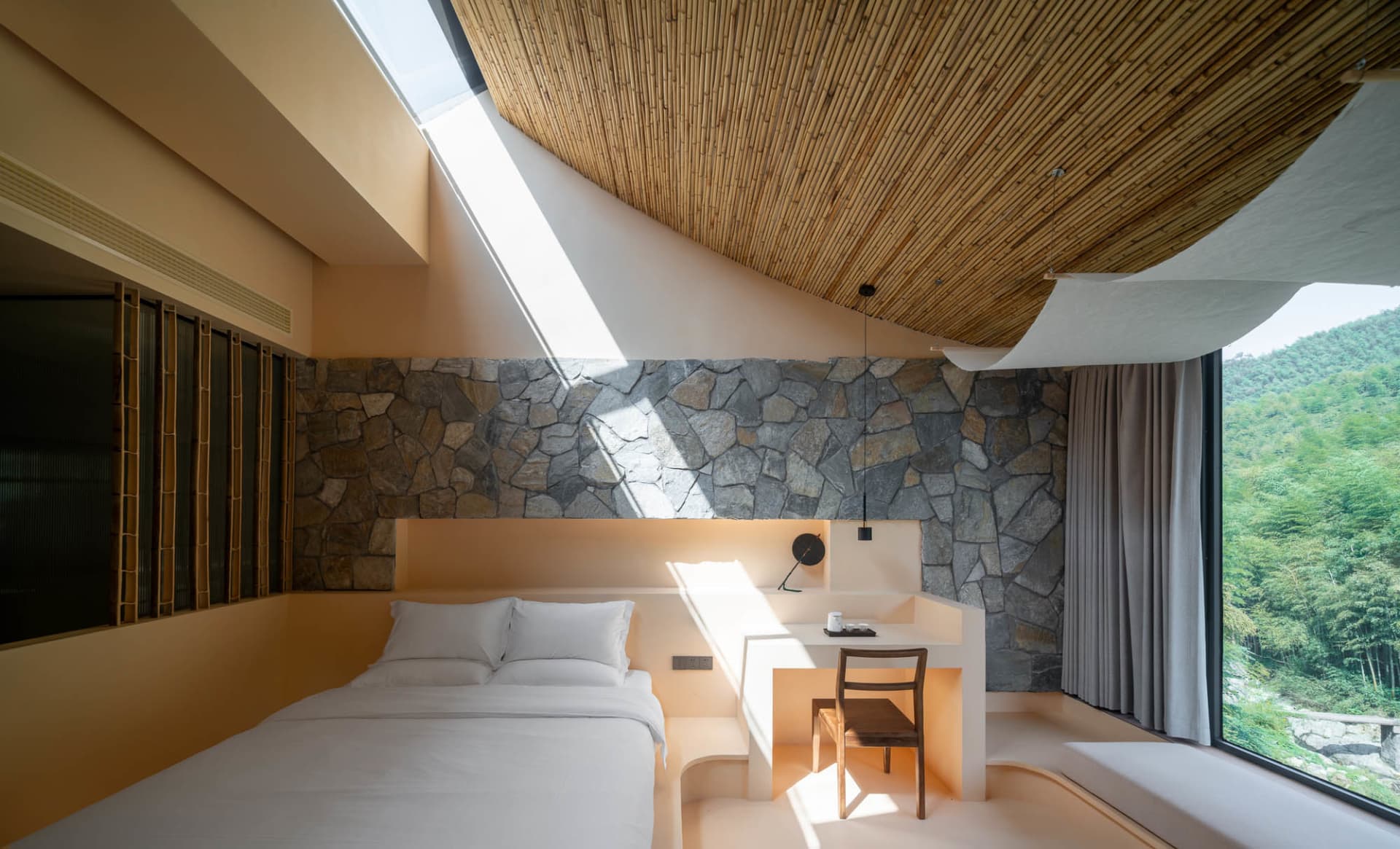 A serene, minimalist bedroom with concrete walls, a skylight, and a view of the mountains.