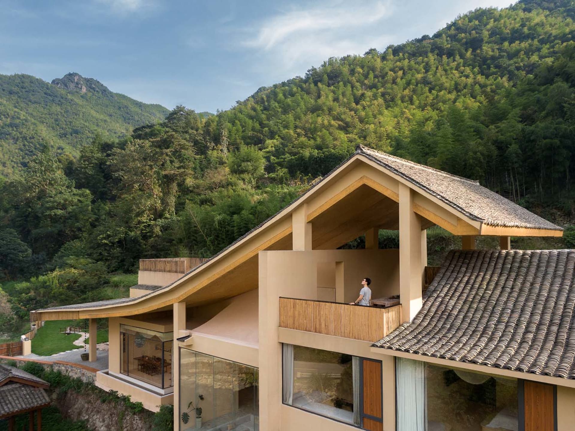 一棟現代住宅，外牆採用木質建材搭配玻璃窗，眺望鬱鬱蔥蔥的森林山坡。