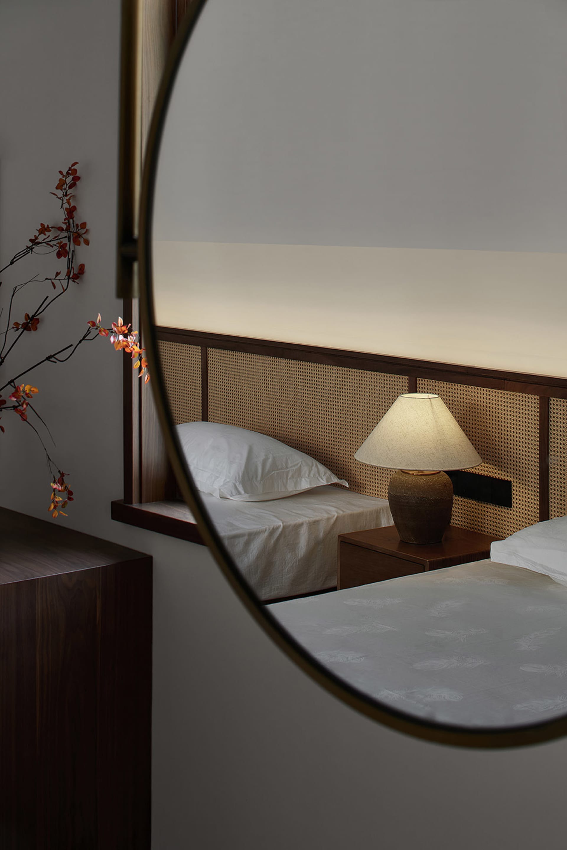 A minimalist bedroom featuring a white bed with a cane-weave headboard and a warm, ambient light.