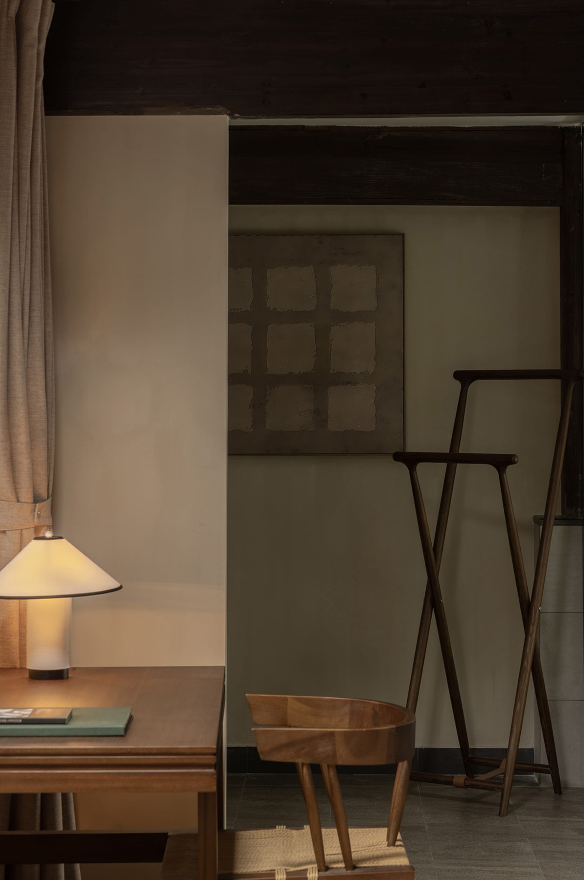 A modern minimalist living room featuring a wooden chair, a simple table lamp, and a minimalist artwork.