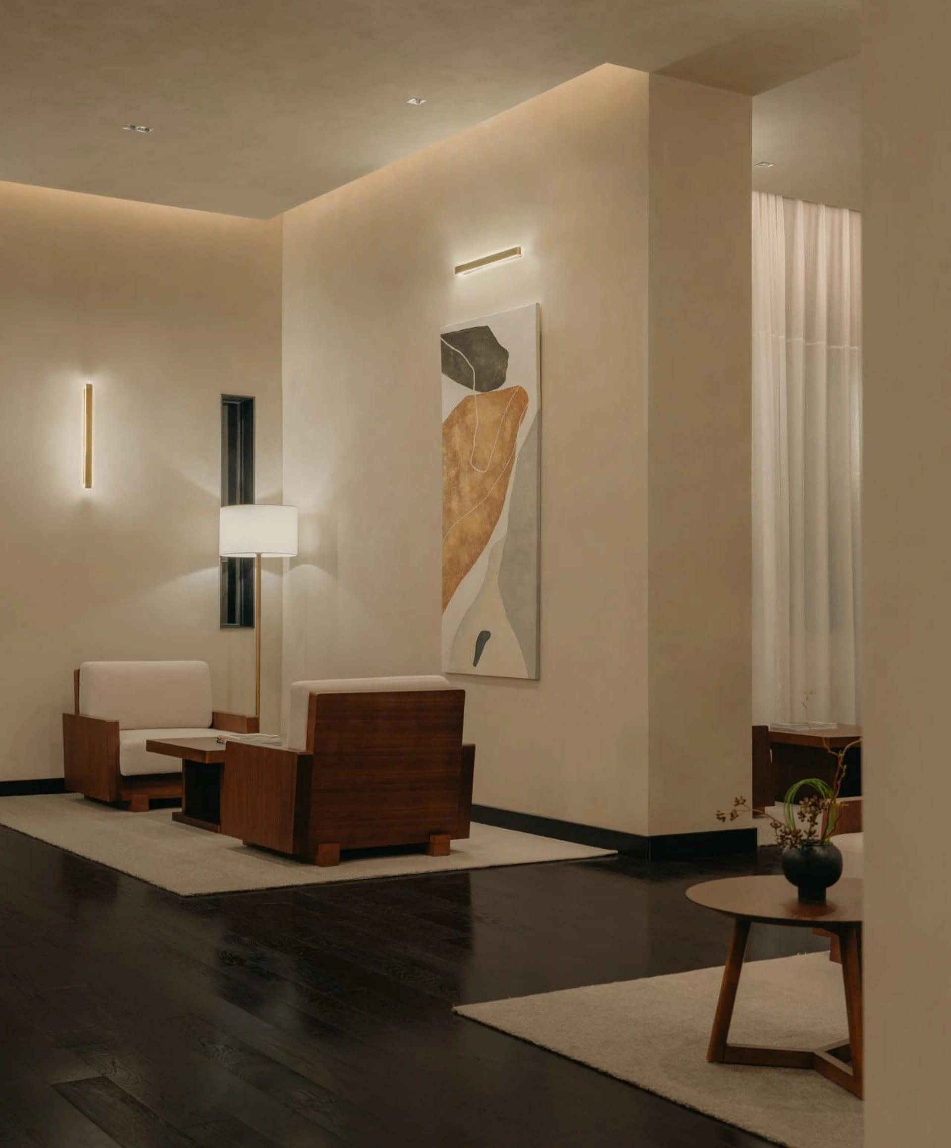 A modern living room featuring wooden furniture, a floor lamp, and a large abstract painting.