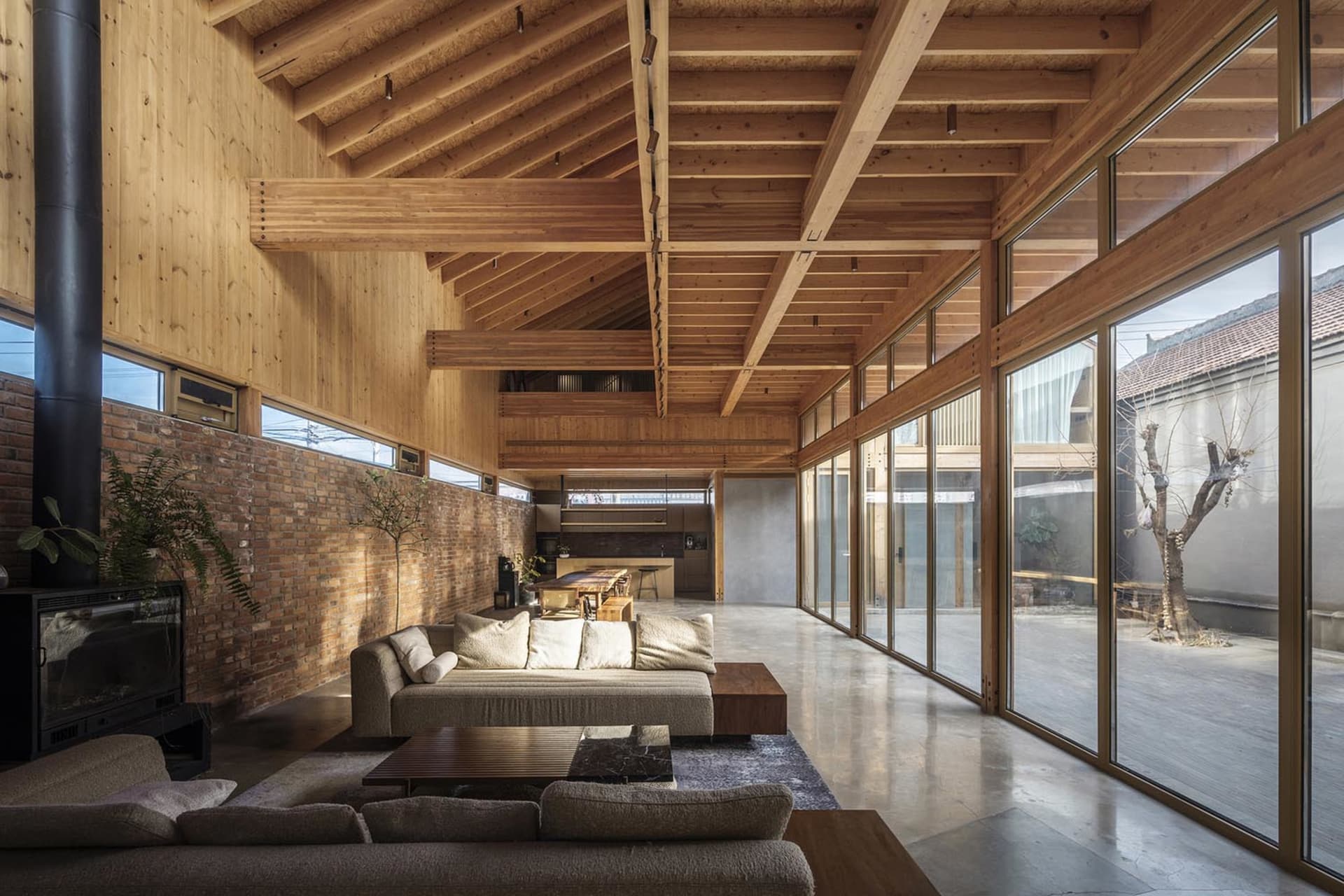 Modern minimalist living room with exposed wooden beams, large glass windows, and a comfortable sofa.