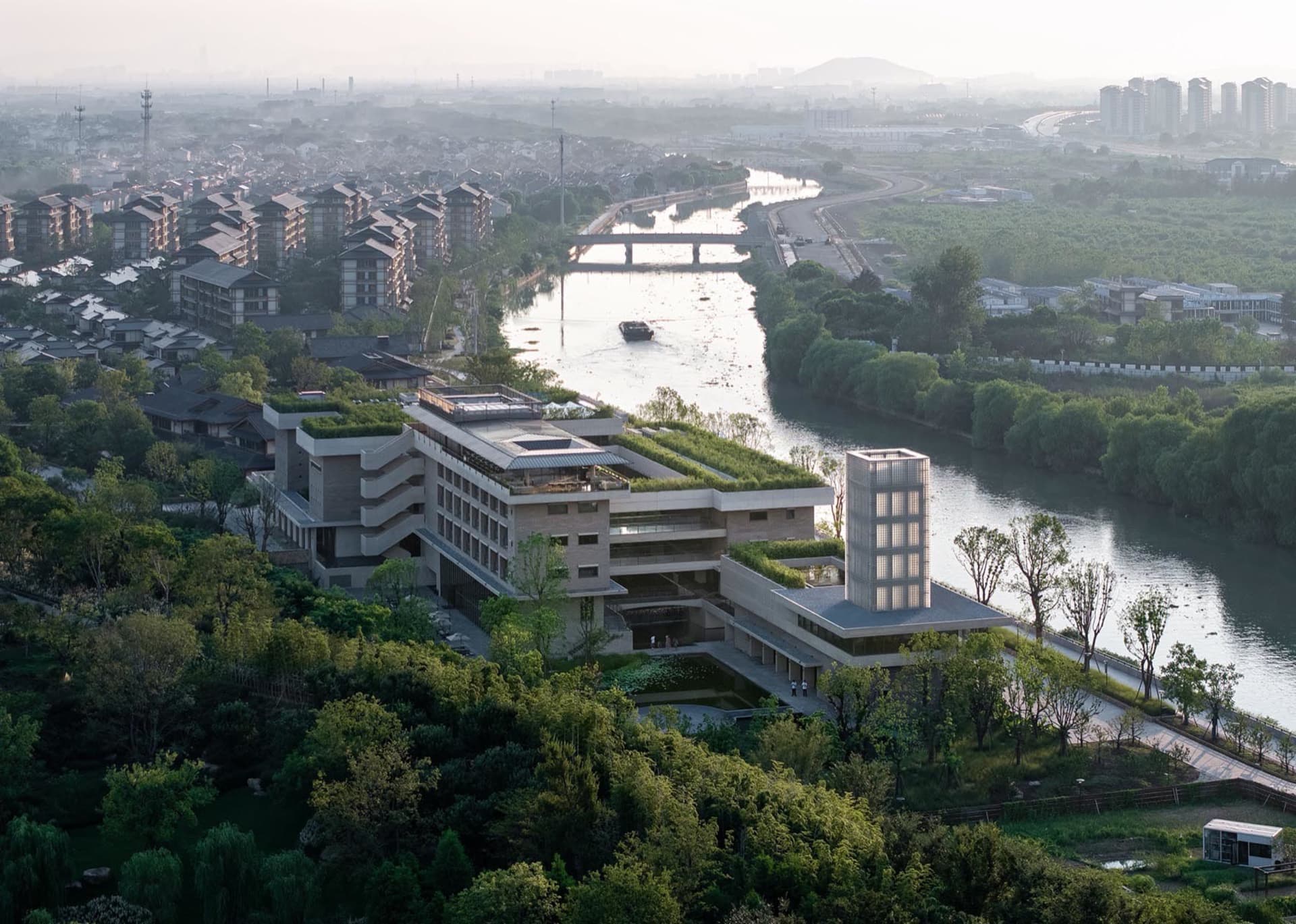A modern office building with a concrete exterior and a landscaped riverfront.