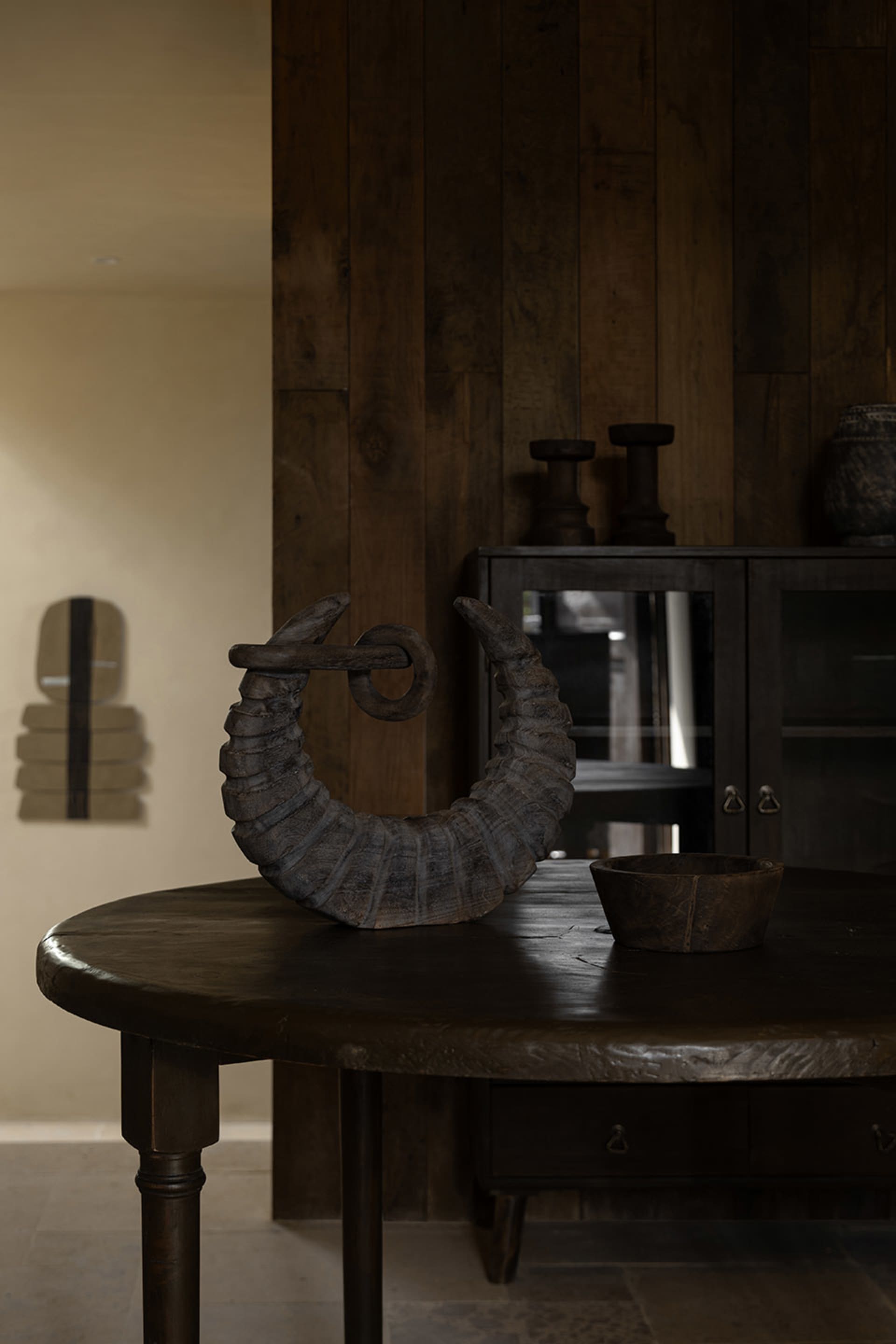 A rustic, dark wooden table with an ornamental piece and a wooden bowl.