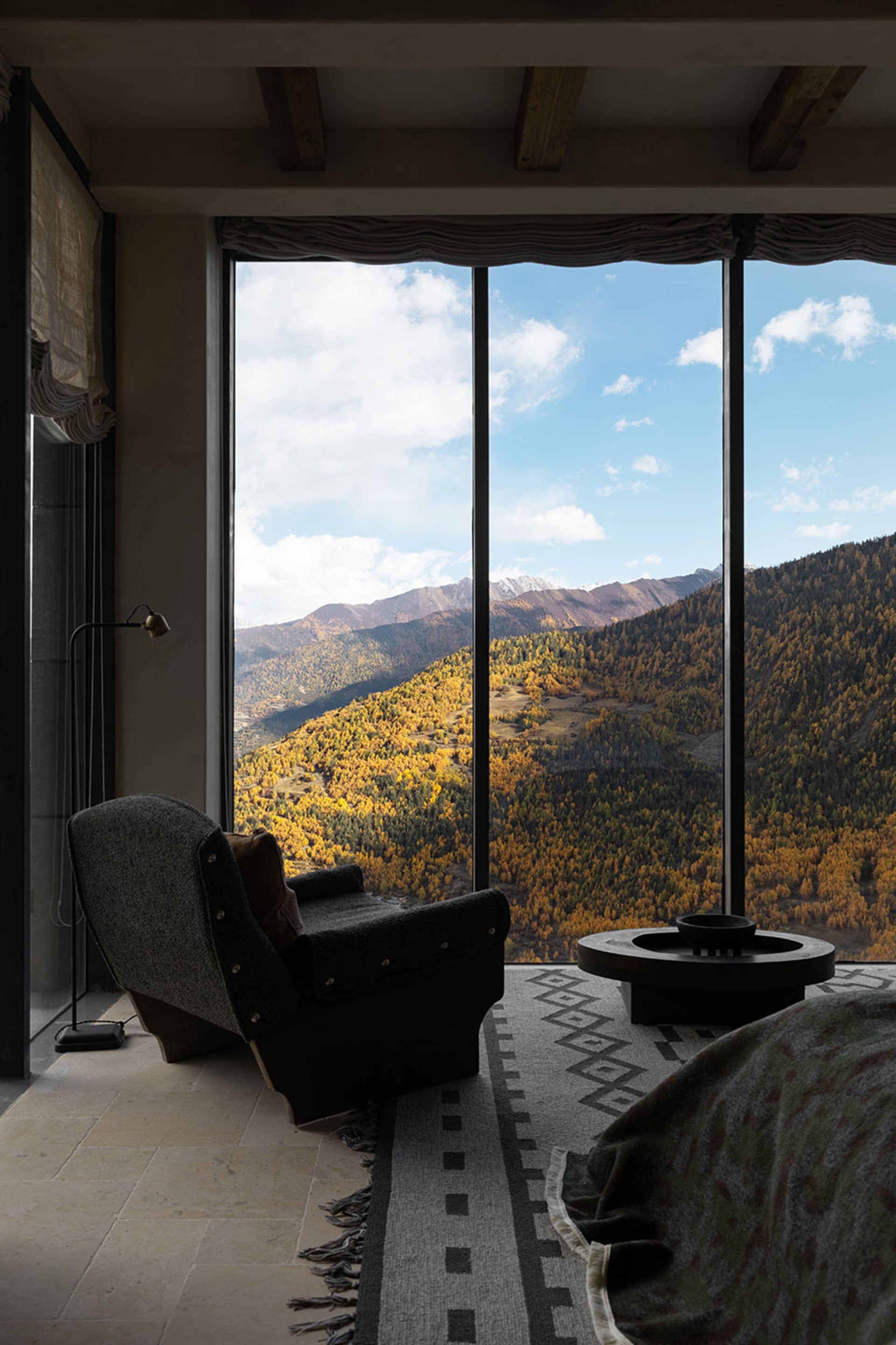 A minimalist living room with a large window overlooking mountains and autumn trees.
