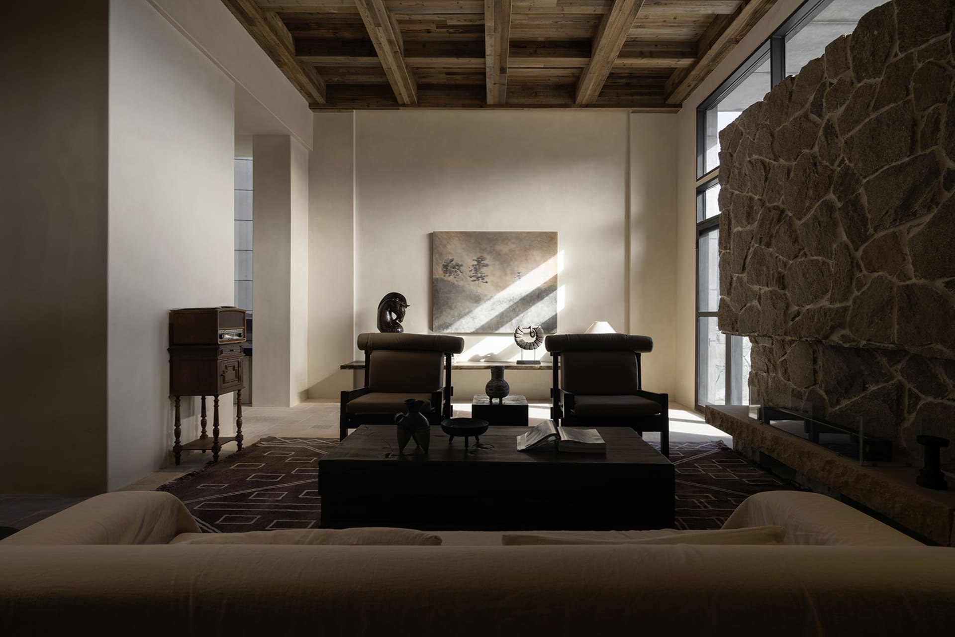 A modern minimalist living room features a stone fireplace, wooden furniture, and fabric seating.