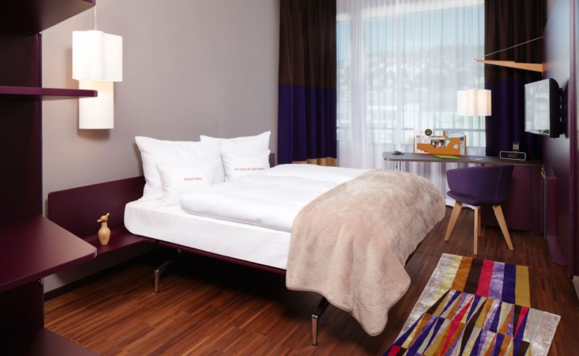 A modern bedroom with a white bed, a colorful rug, and purple accents.