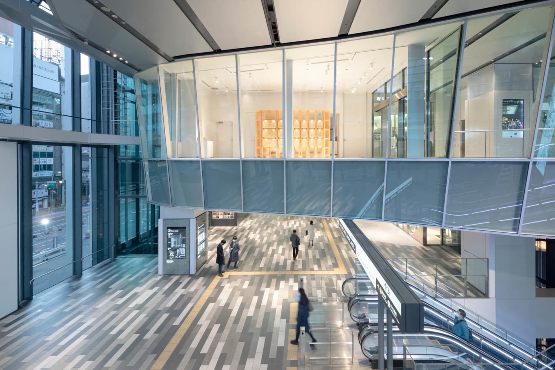 Modern shopping center interior with glass walls, concrete floors, and tiled accents.