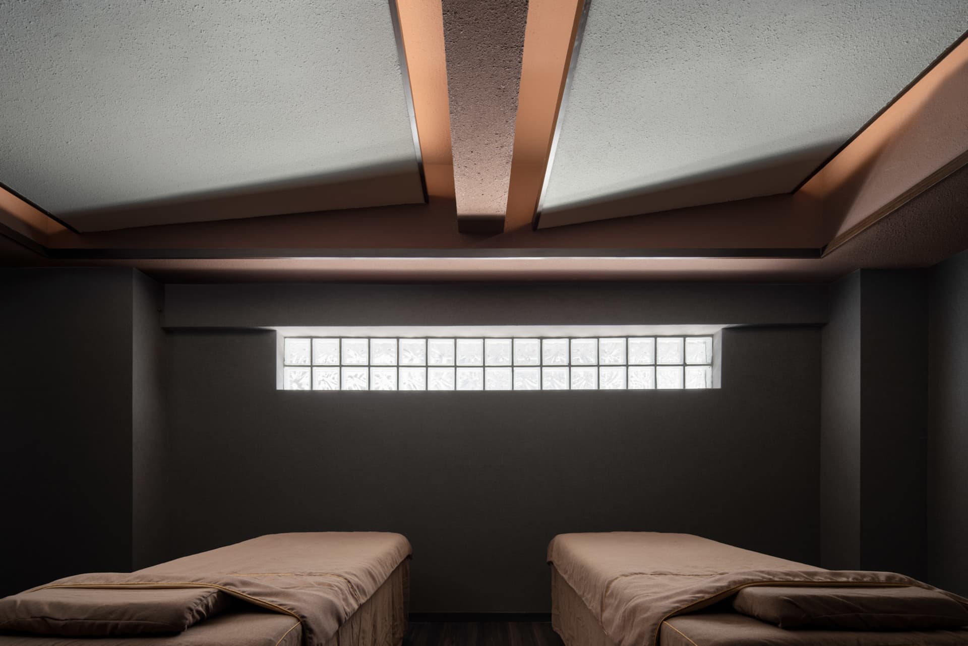Industrial-style spa treatment room featuring a glass block wall and two massage tables.