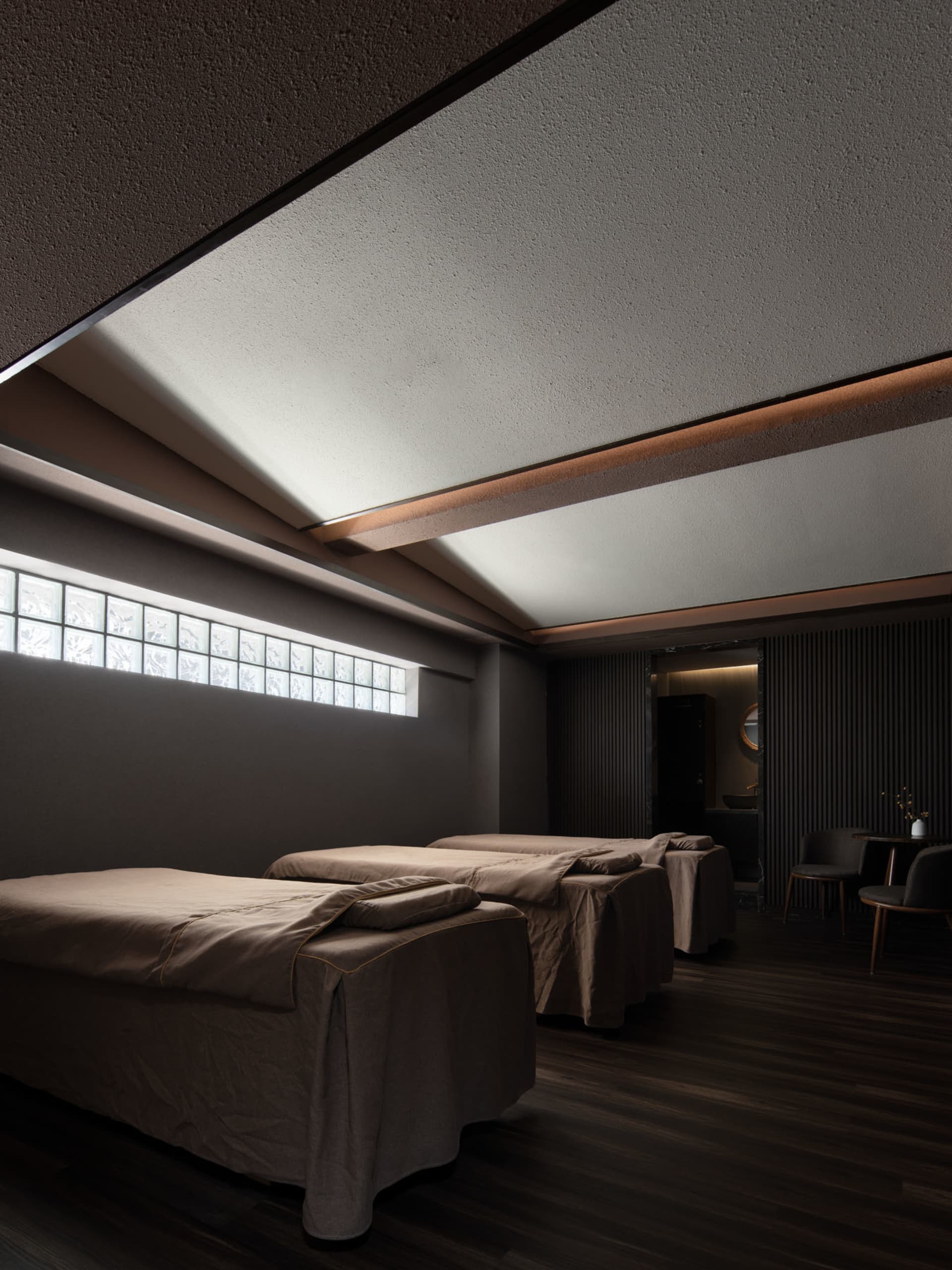水療室內有三張按摩床，床面覆蓋棕色布料，室內色調深沉，並設有小窗搭配方格玻璃。