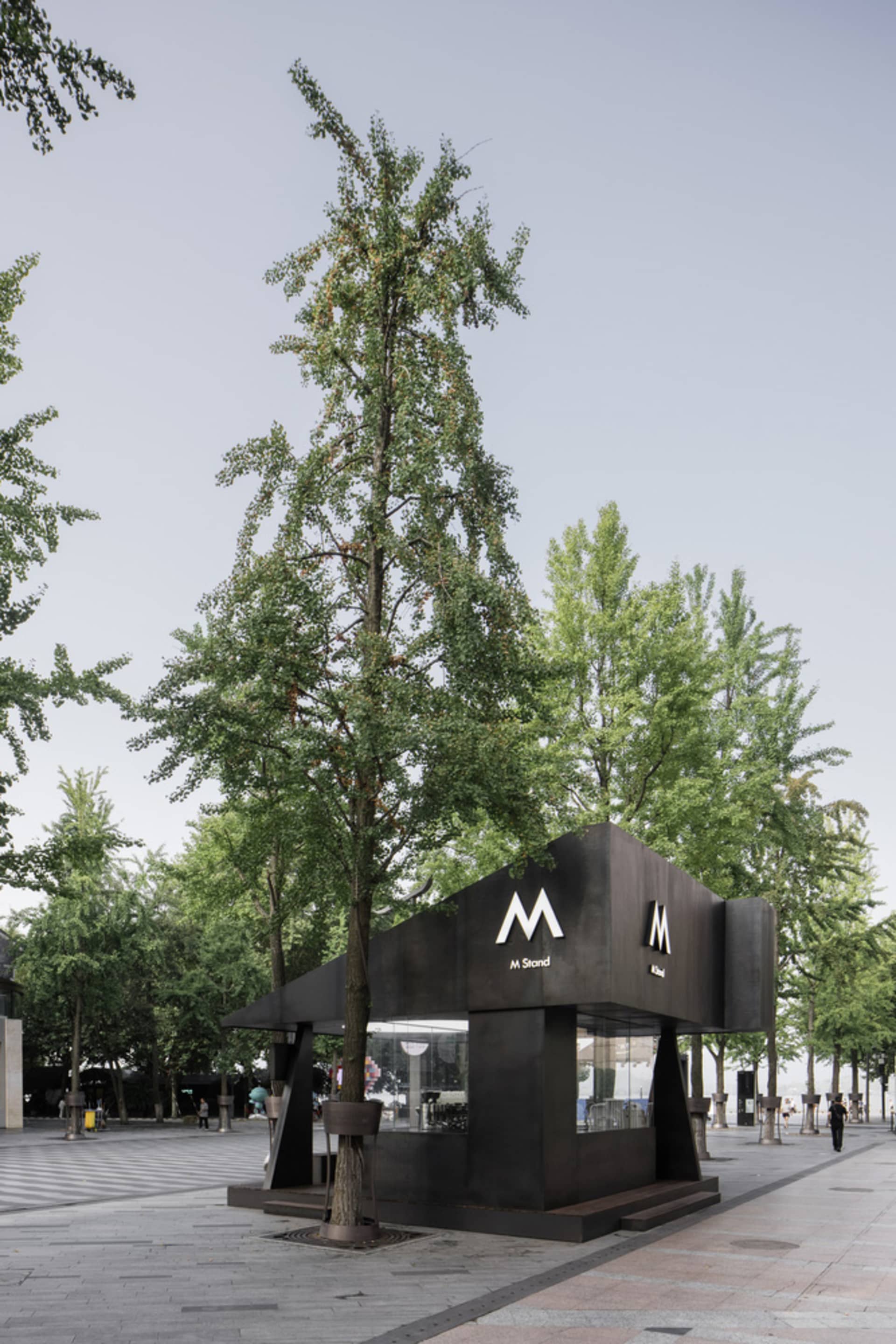 Black metal food vendor stand with an 'M' logo and a modern exterior design in an open urban area.