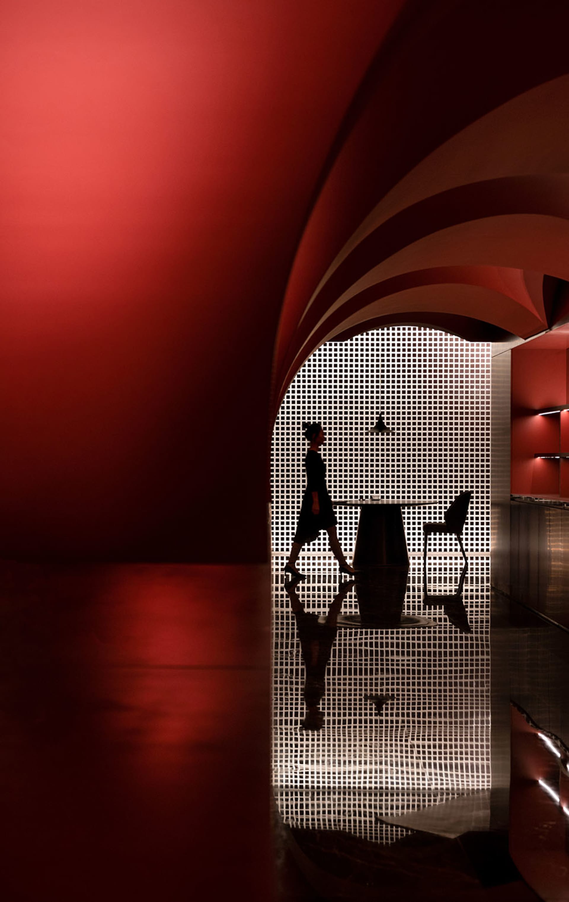 A modern space with red walls and a black grid pattern on the floor and ceiling, featuring a woman walking through the archwa