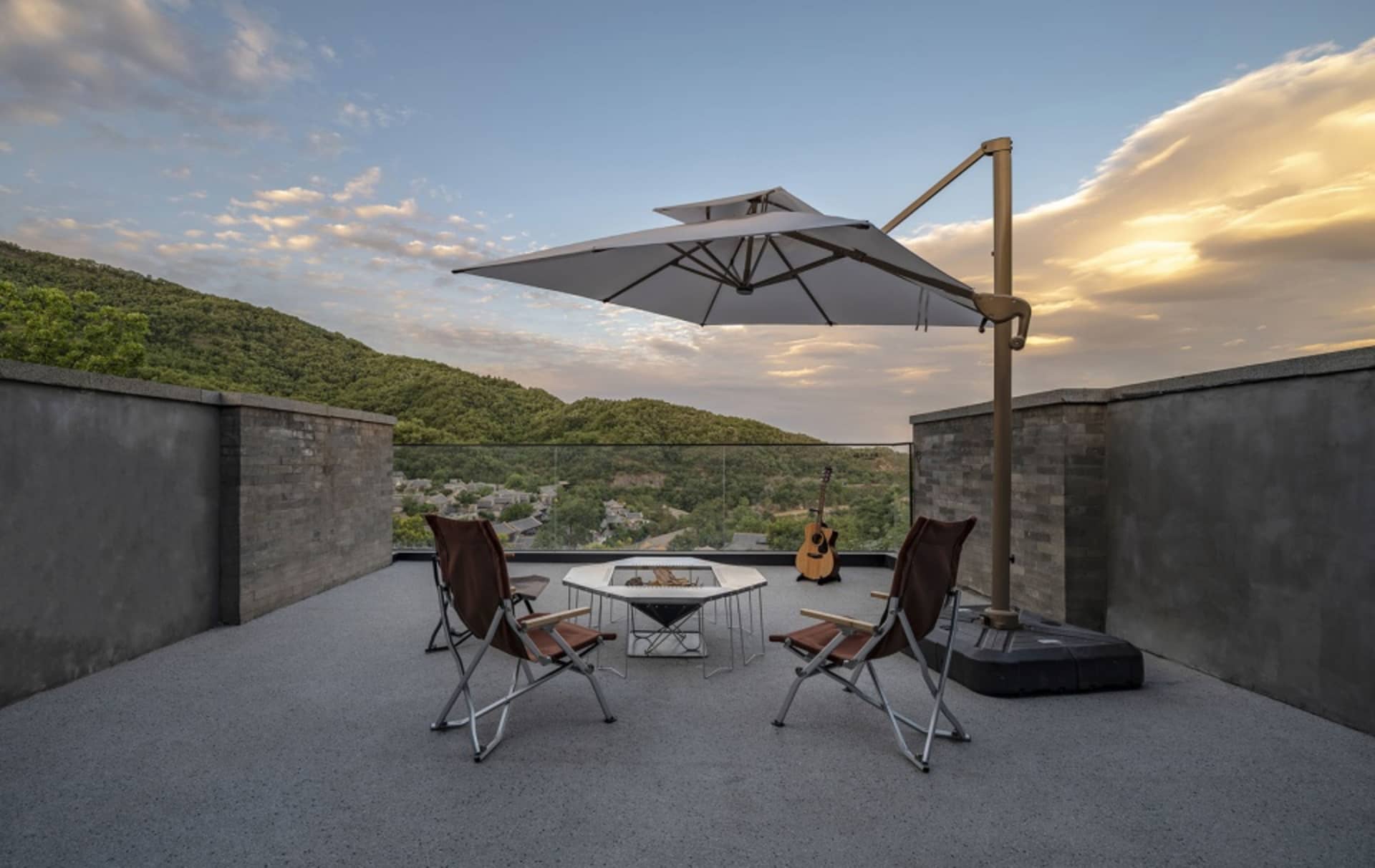 Modern outdoor living space with concrete flooring, steel barrier, glass railing and brick cladding.