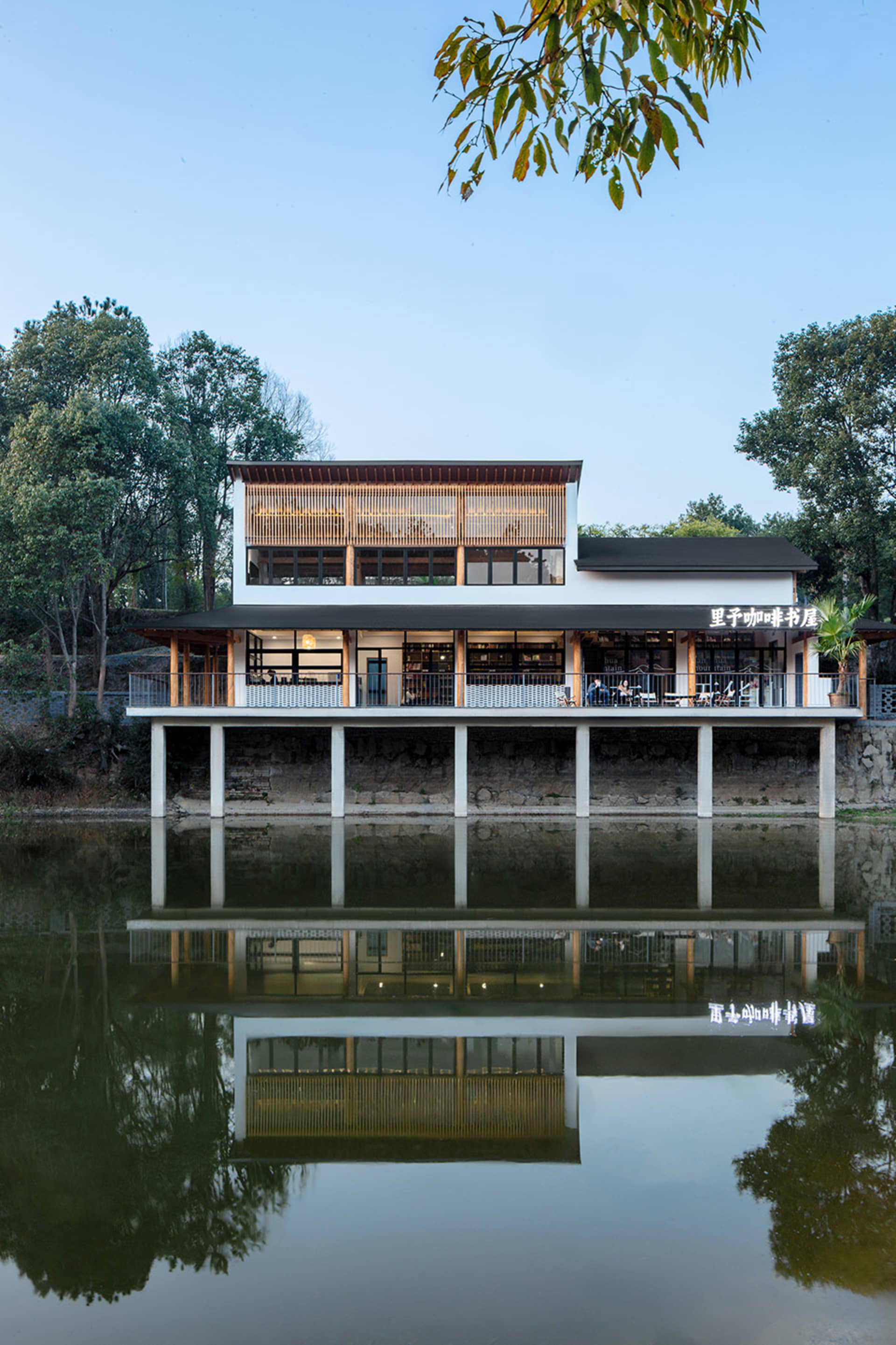 Modern restaurant building with wooden accents and concrete columns surrounded by calm water