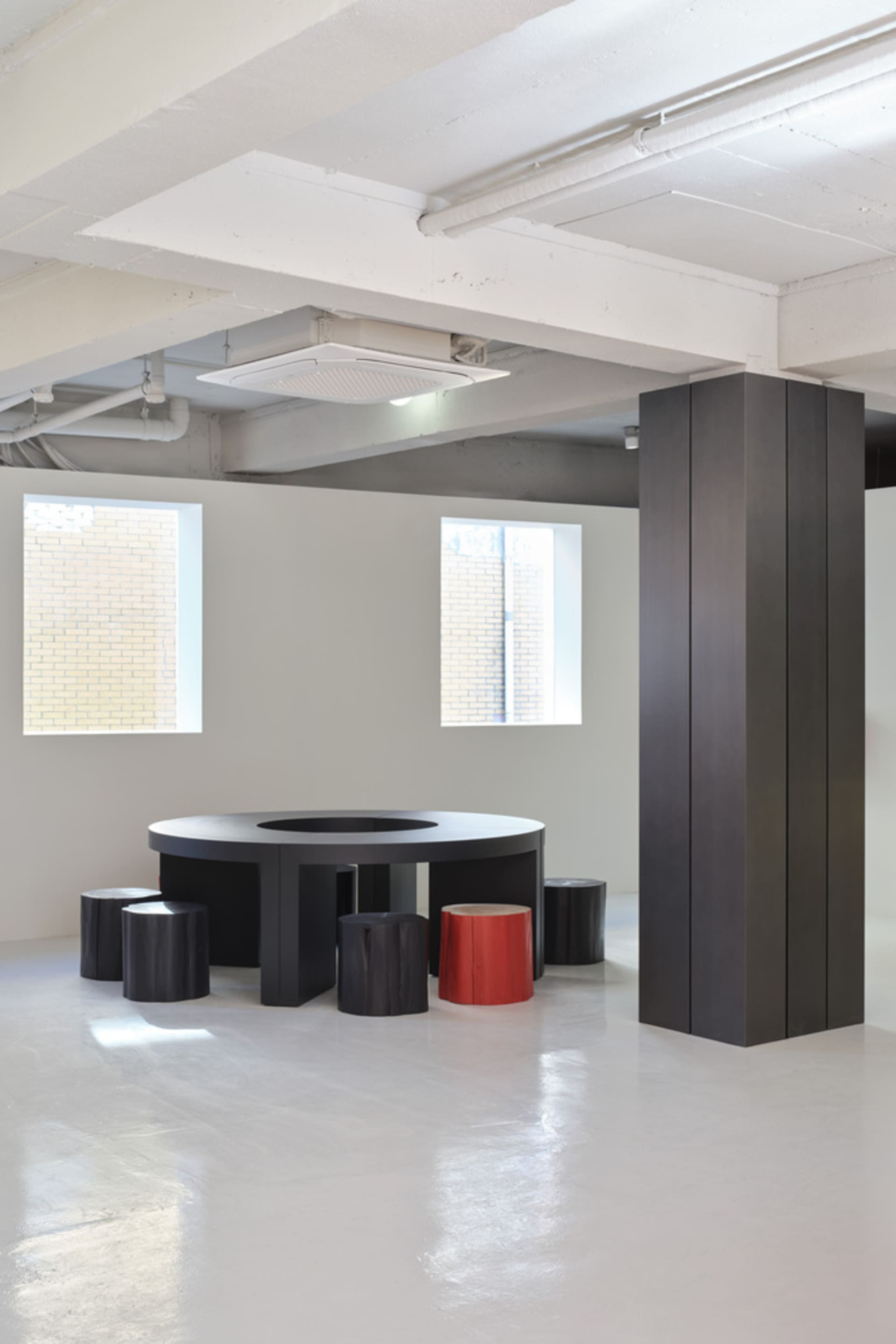 A modern industrial conference room featuring a black circular table, red stool, and concrete space.