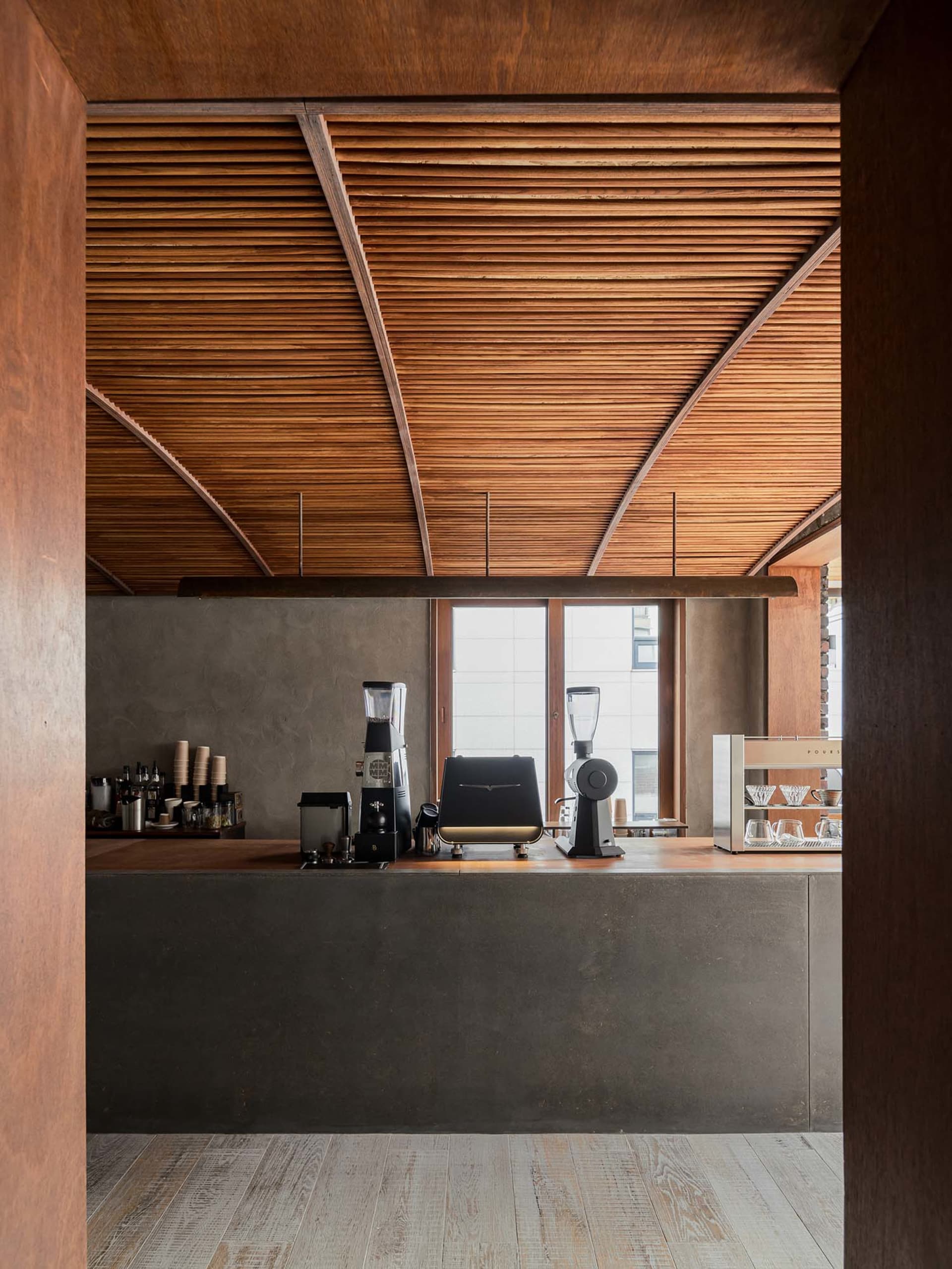 A modern, industrial-style coffee shop counter with a wooden ceiling and minimalist design.