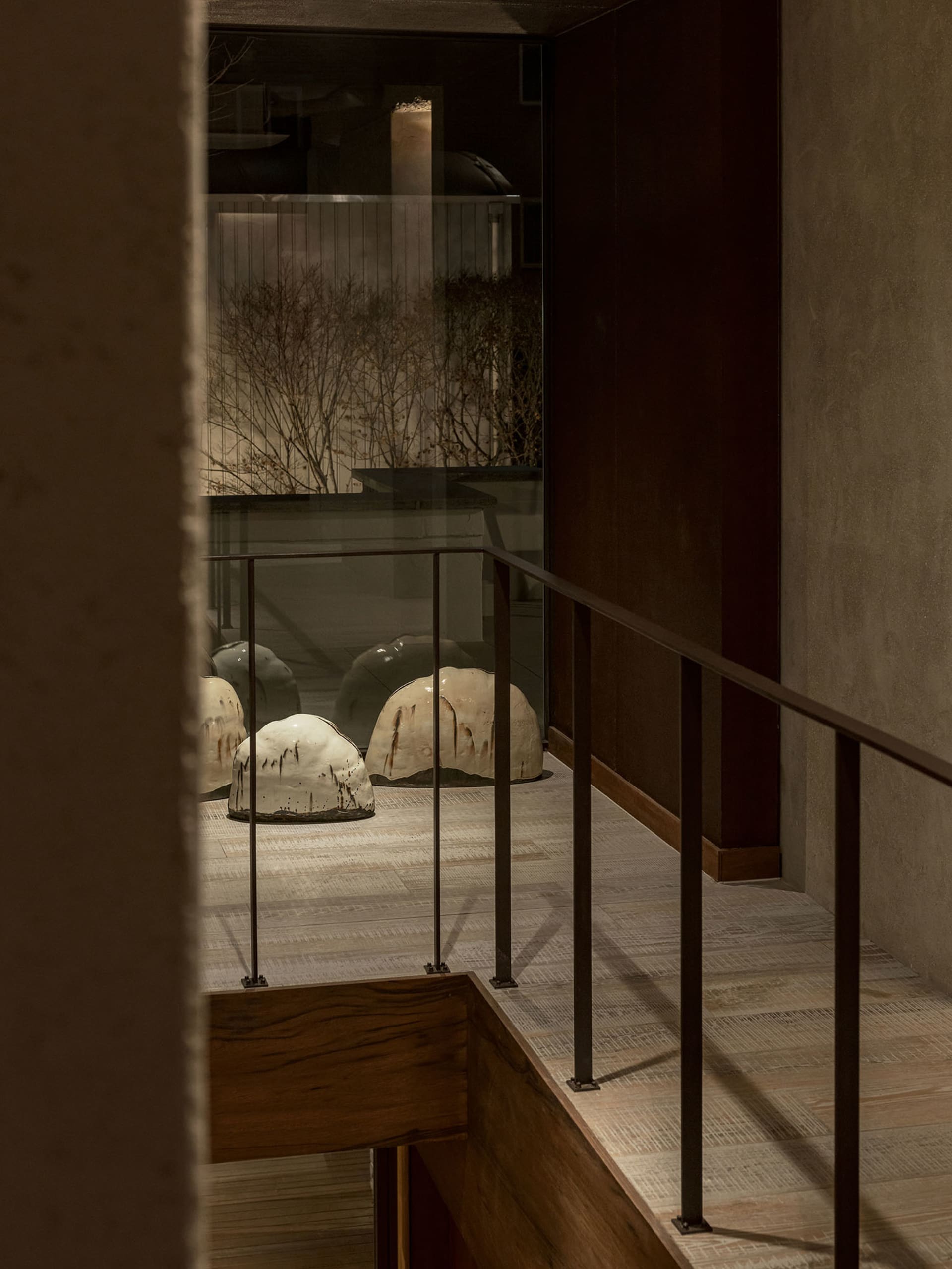 A staircase with a glass railing overlooking ceramic sculptures and a landscaped area with trees and plants.