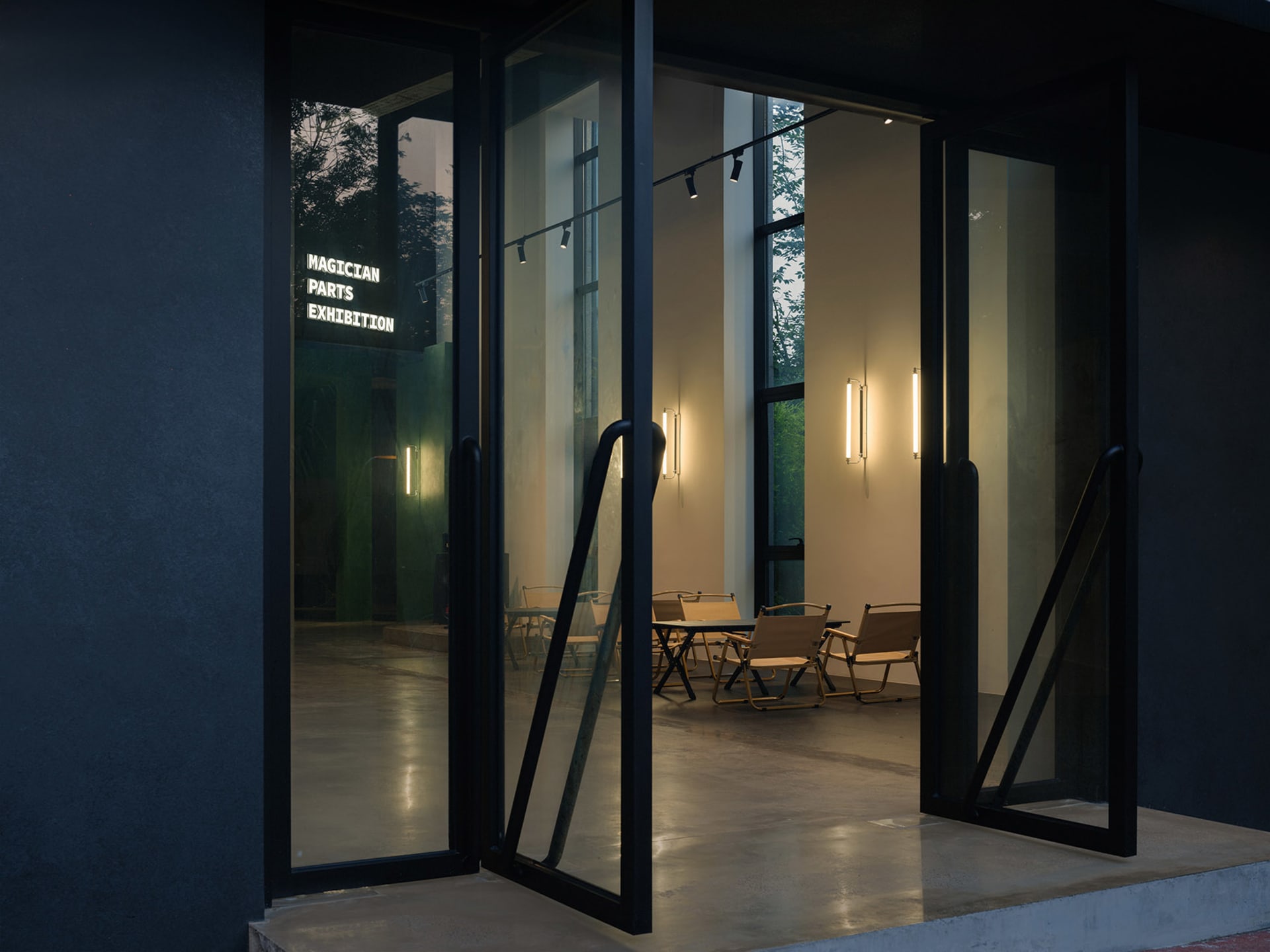 An exhibit space accessible through glass doors with ambient lighting and a view of outdoor seating.