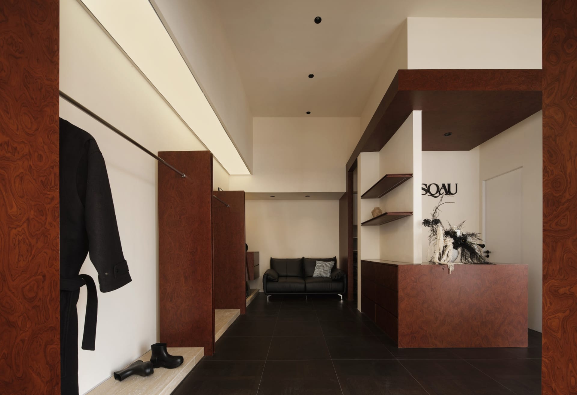 A modern clothing store with wooden paneling, featuring a minimalist design with sleek black furniture and a wooden reception