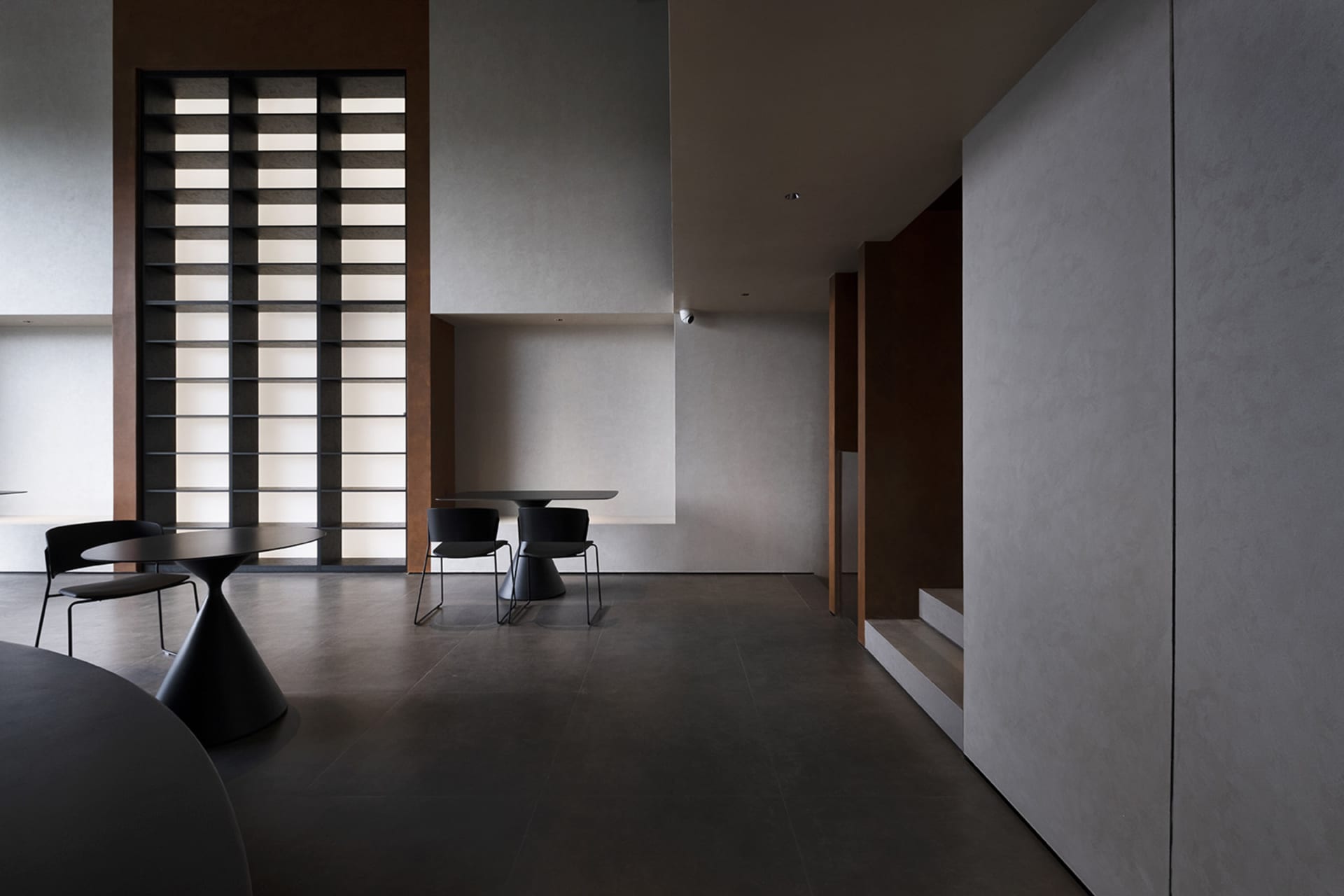 Modern, minimalist interior with concrete walls and floor, featuring a sleek, black dining table and chairs.