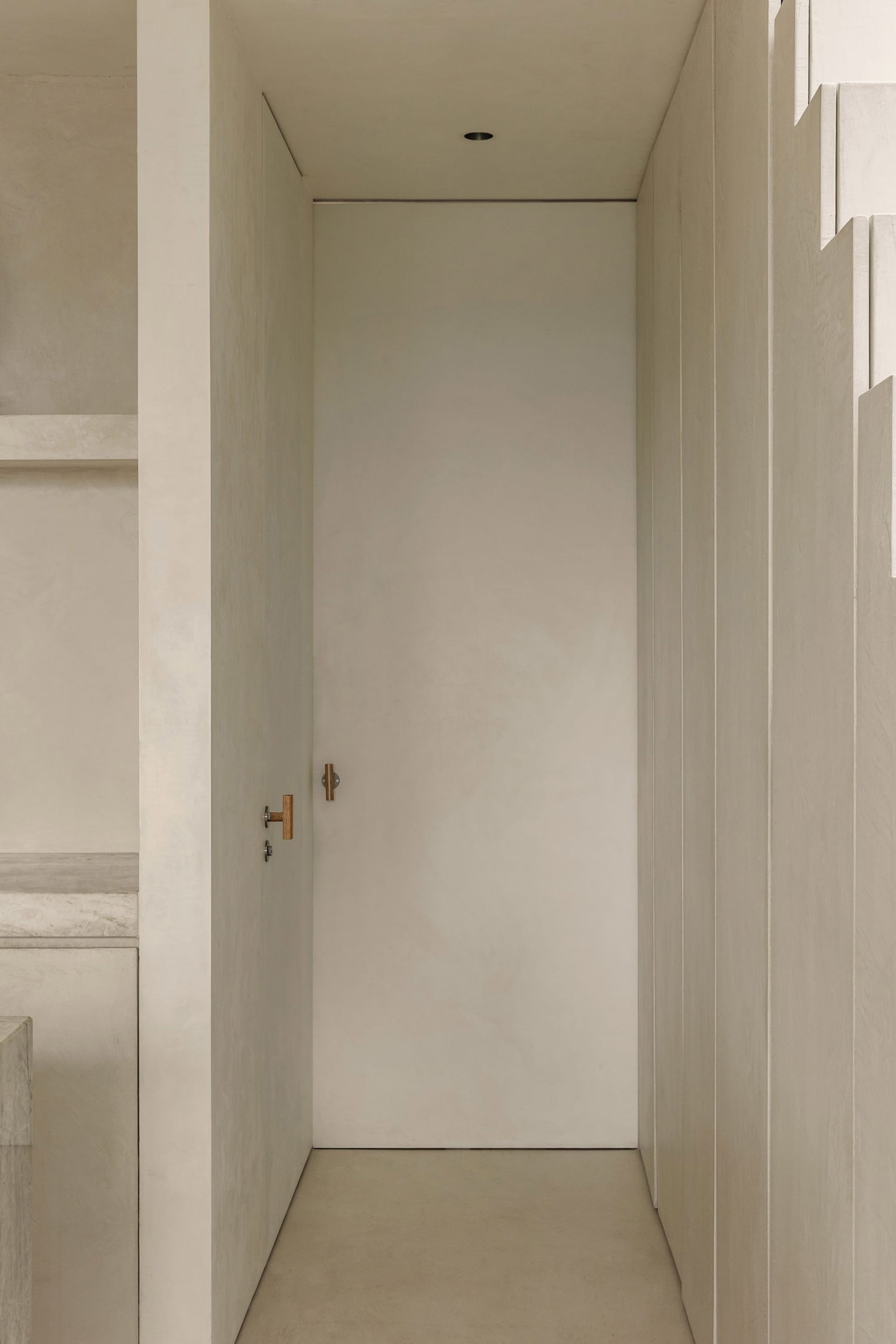 A minimalist doorway made of concrete with a simple wooden handle.