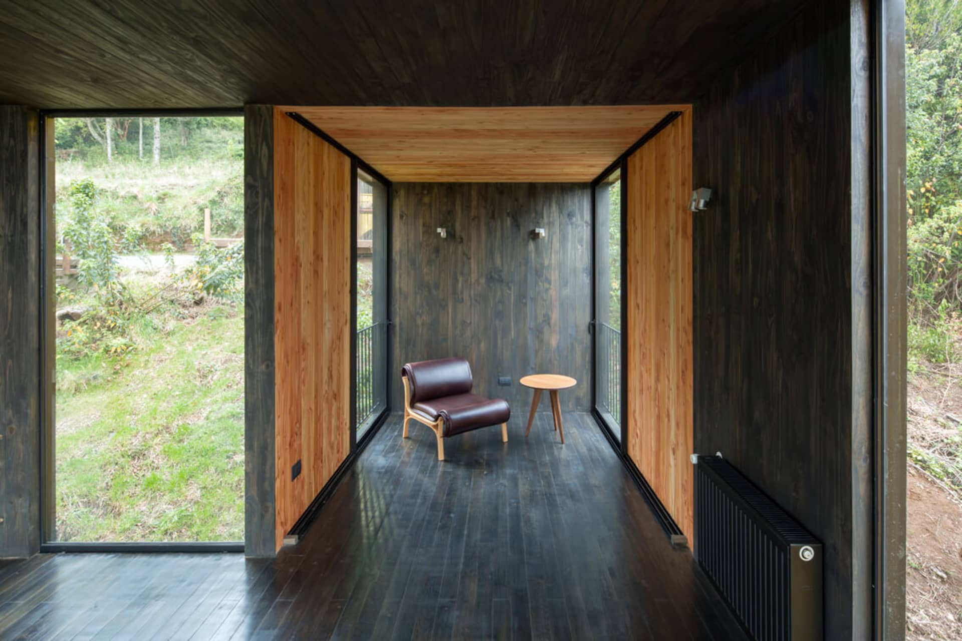 A minimalist room with wooden floors, walls, and panels, featuring a brown leather chair and small wooden table.