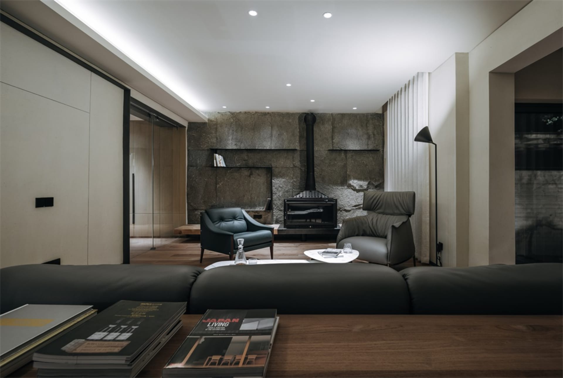 A modern living room with concrete walls, black leather armchairs, and wood flooring.