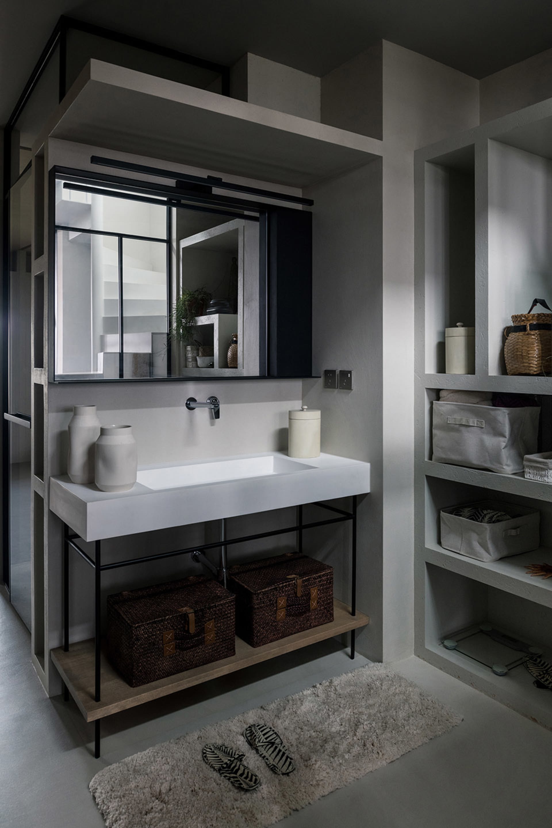 A modern minimalist bathroom with a concrete sink, metal faucet, and woven baskets under the counter.