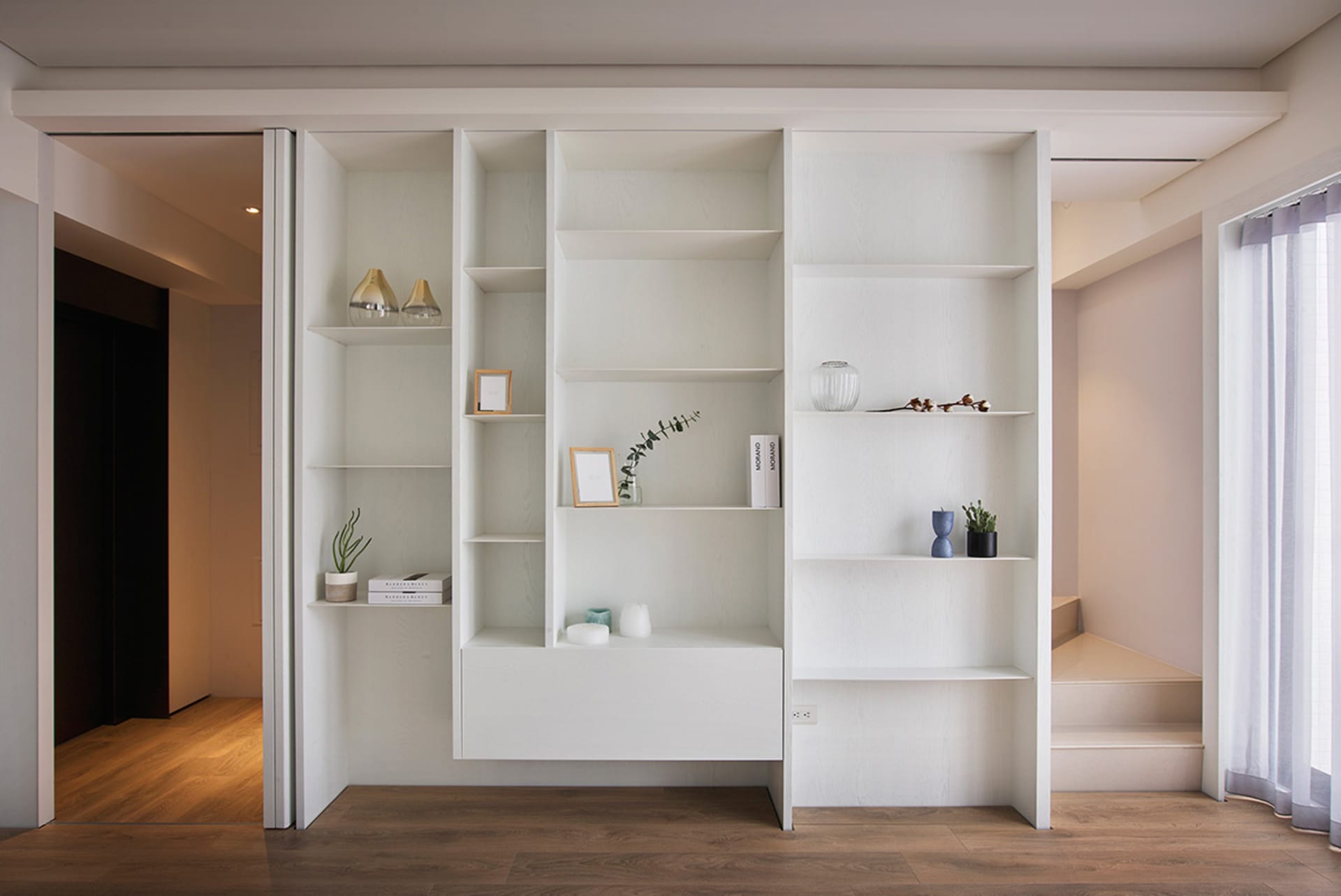 A minimalist living room with a white floating entertainment center displaying various decorative items, set against a wooden