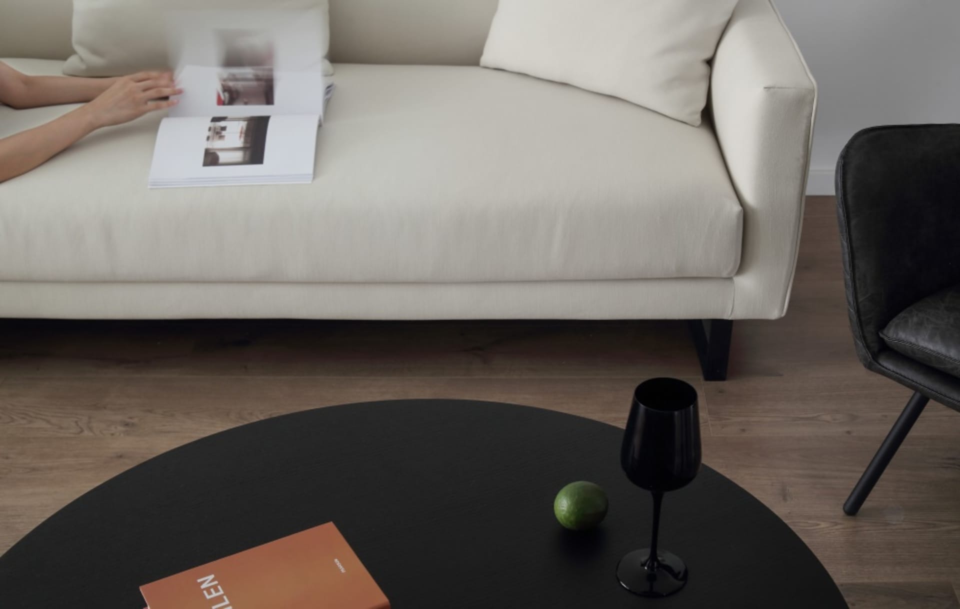 A modern living room with a white sofa, black coffee table, and black leather chair.