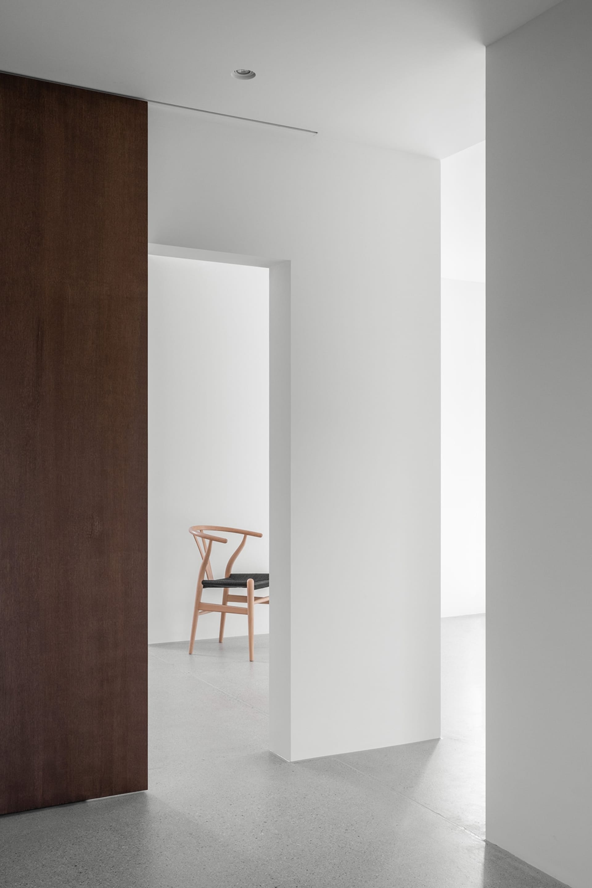 A minimalist interior space featuring concrete walls and floors, with a single wooden chair.
