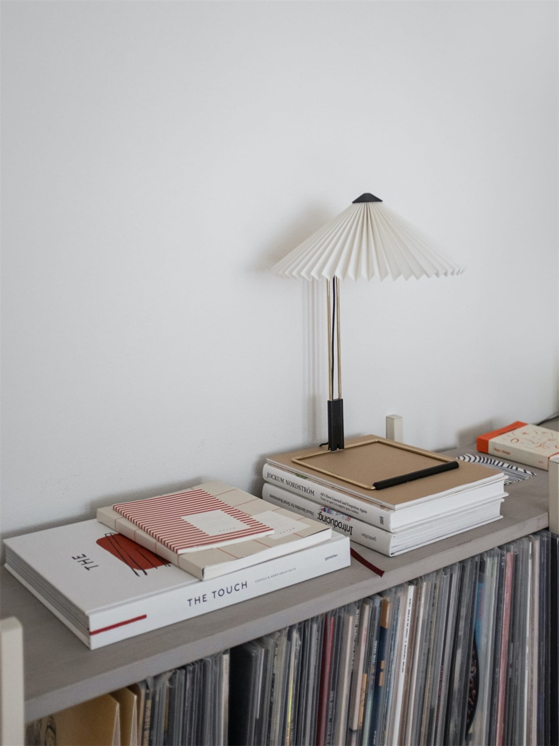 A minimalist shelf made of wood with books, a frame, and a table lamp.