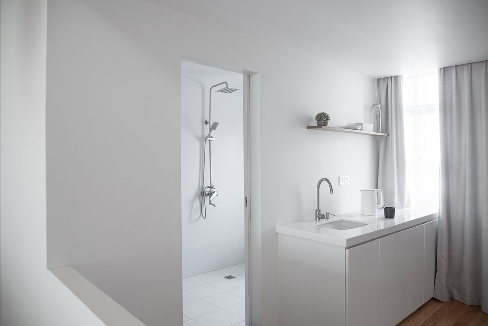 A minimalist kitchen with a white countertop, cabinets, and floor, featuring a window with sheer curtains.