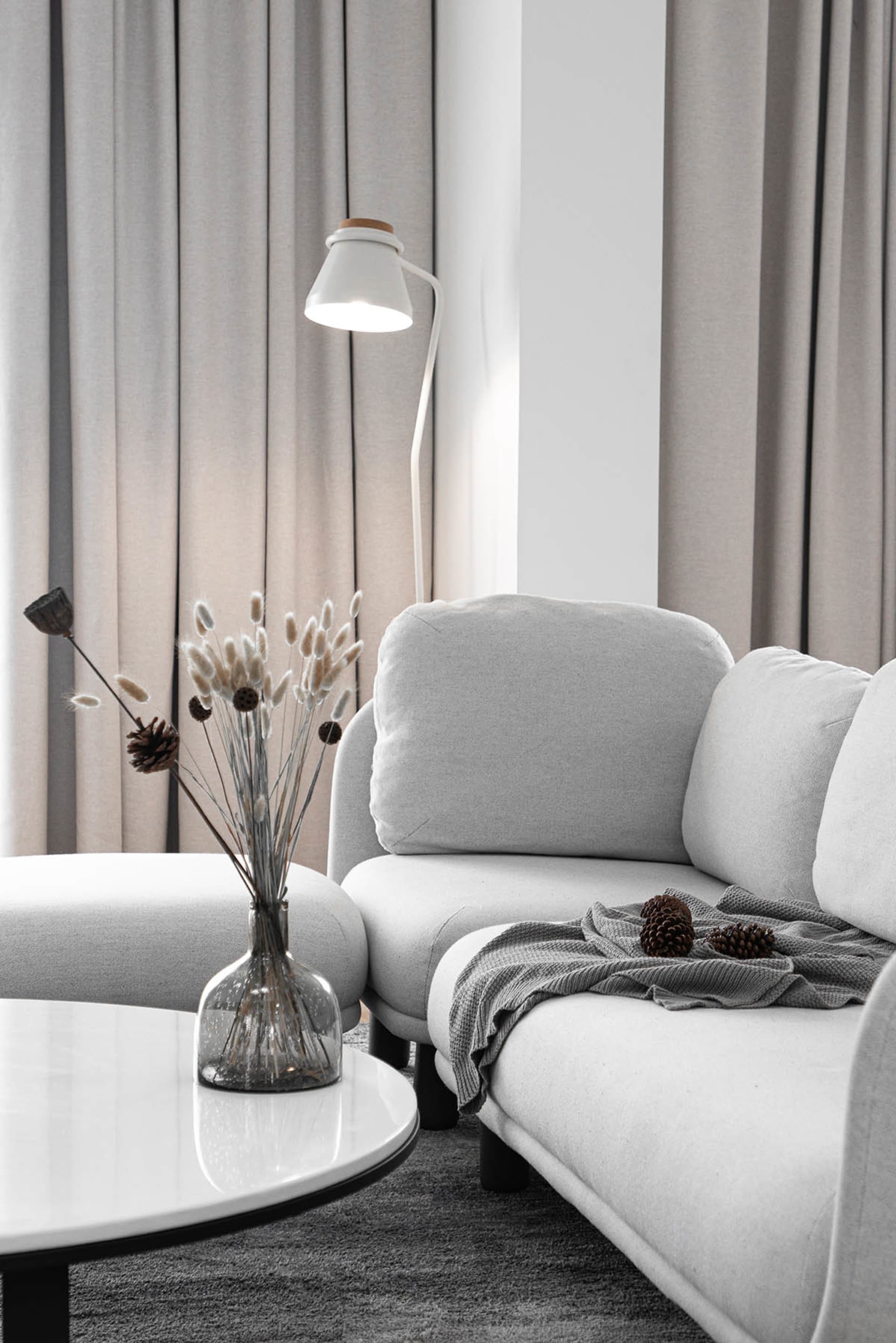 Modern grey living room with minimalist design, featuring a comfortable textile sofa, glass vase with dried flowers, and a sl