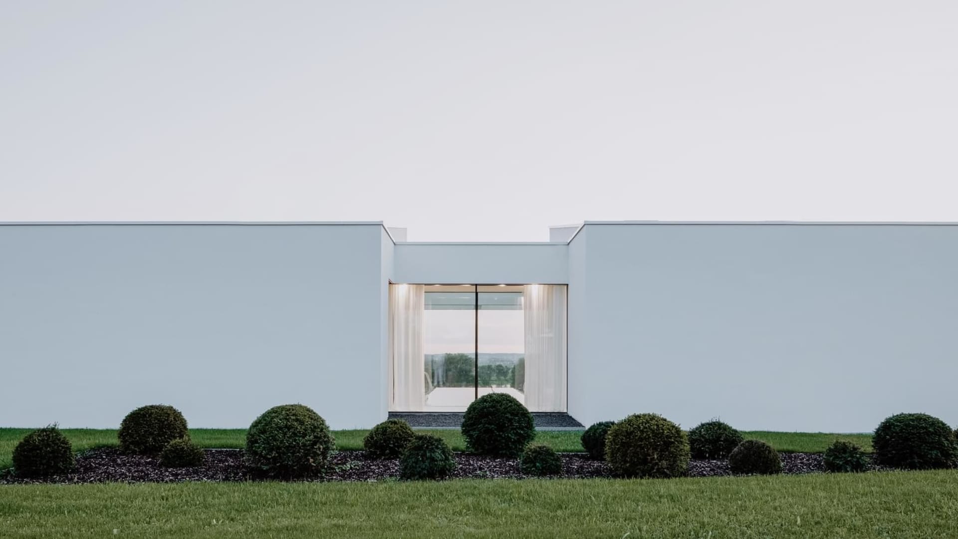 Modern residential exterior with minimalist design featuring white stucco walls and large glass window.