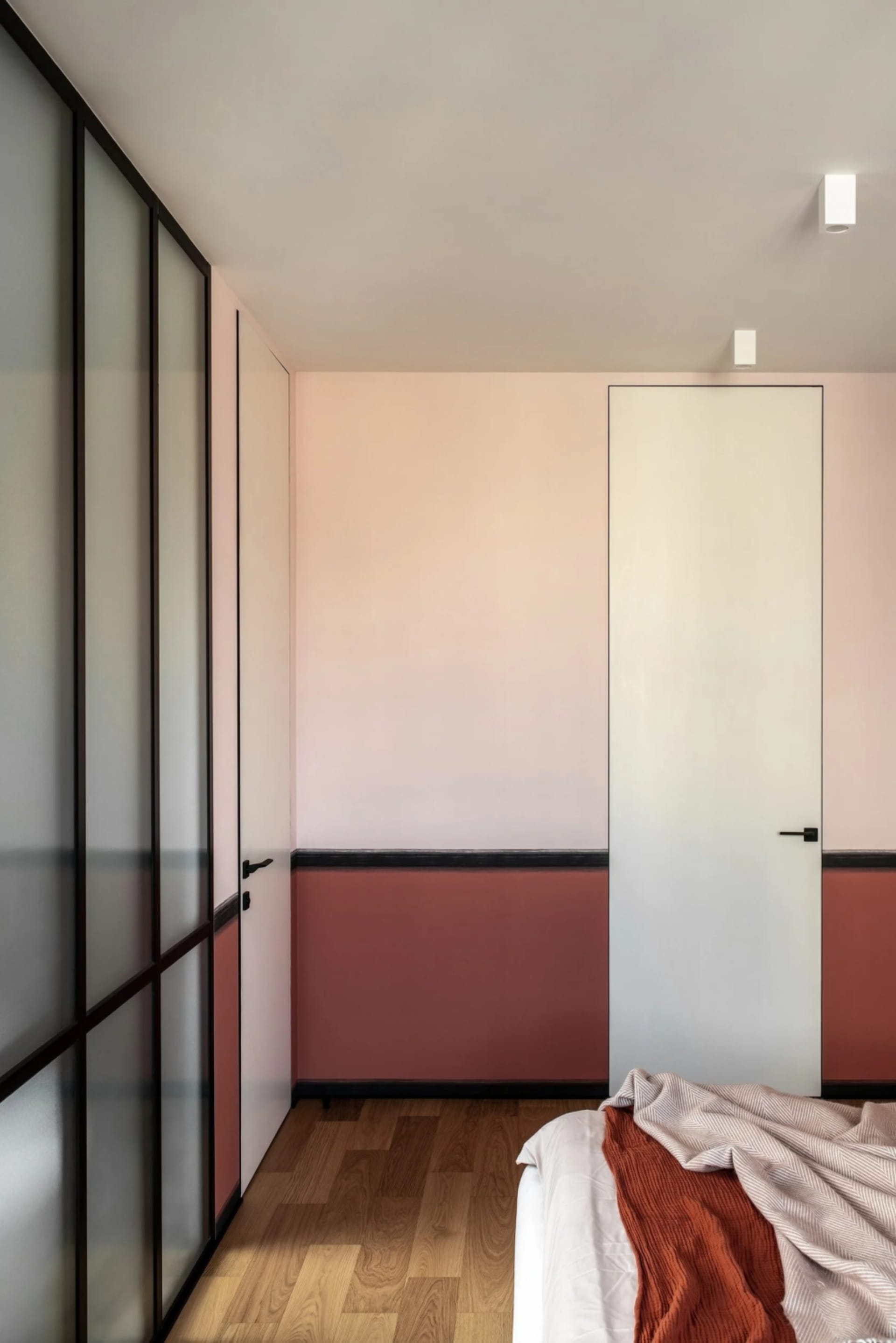 A minimalist bedroom with wooden floors, glass doors, and a red blanket on the bed.